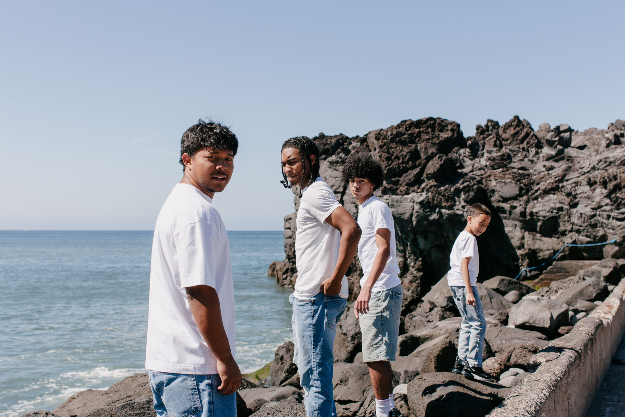 Four brothers standing in a line on the rocks, looking back over their shoulders, the Atlantic to the left, Praia Formosa, Madeira