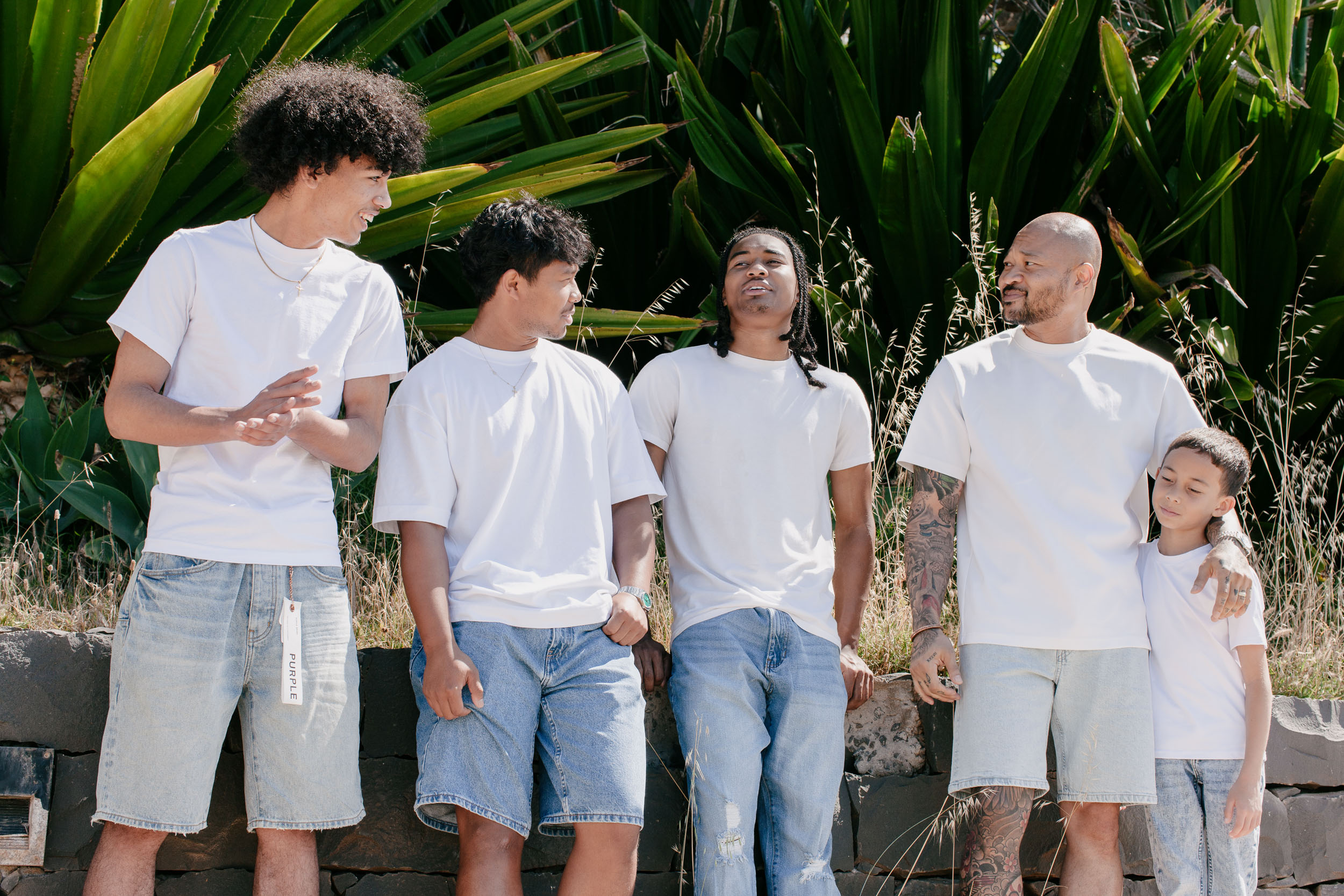 Father and four sons along a low stone wall, talking and laughing together, agave and grass behind, Praia Formosa, Madeira