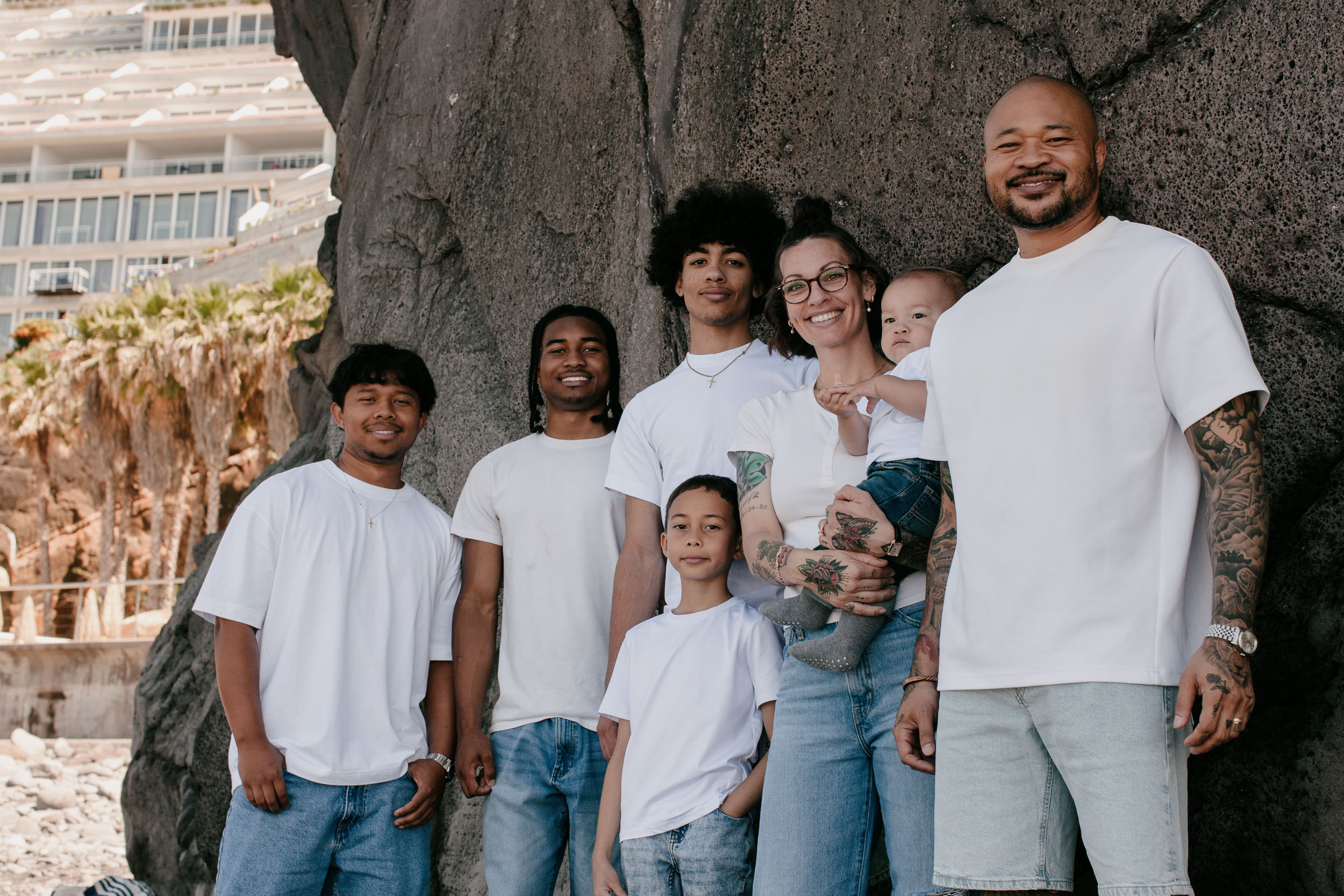 Family of seven beside a large volcanic boulder, palms and the seafront promenade behind, Praia Formosa, Madeira
