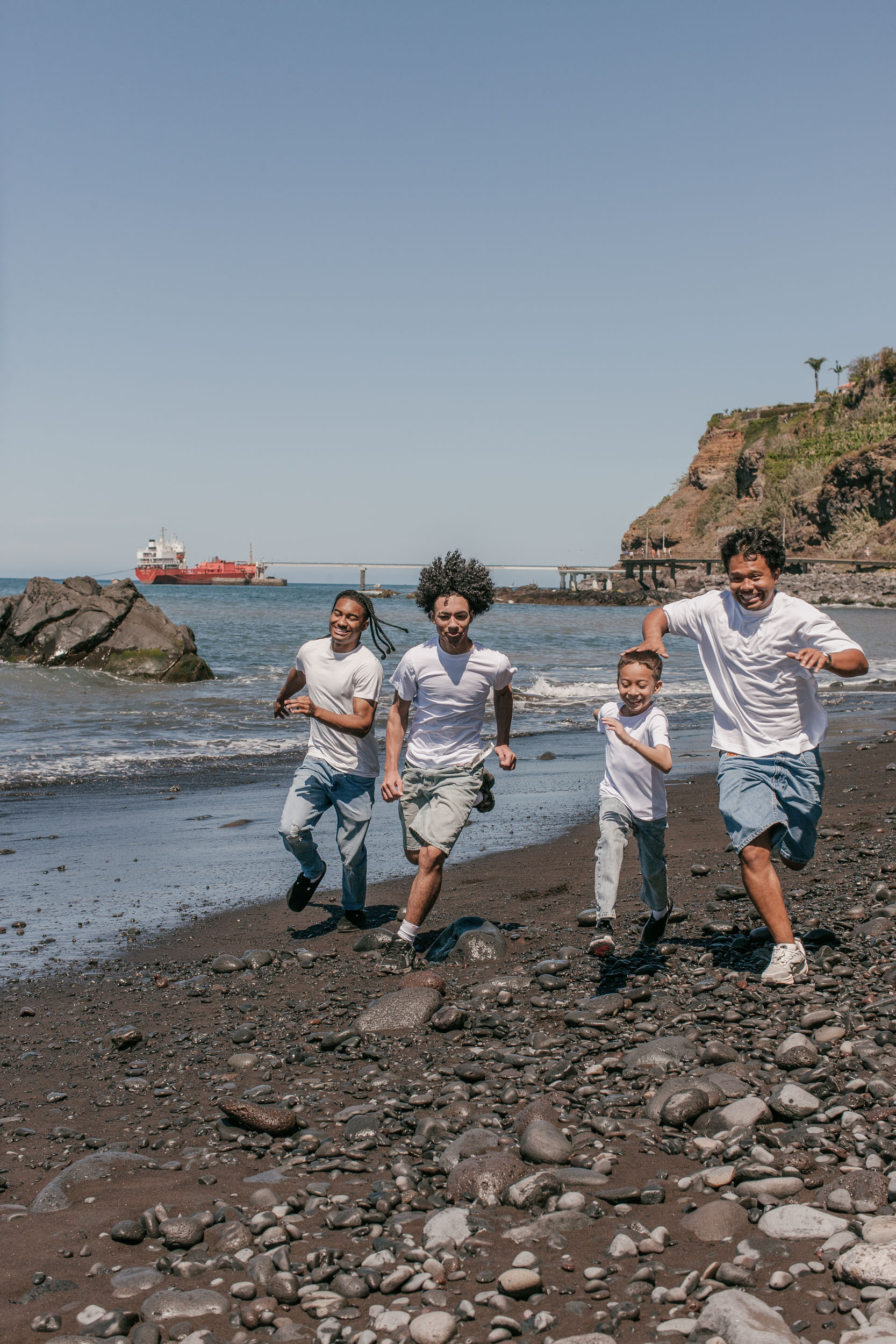 Four brothers running toward the camera along the beach, a cargo ship and headland behind, Praia Formosa, Madeira