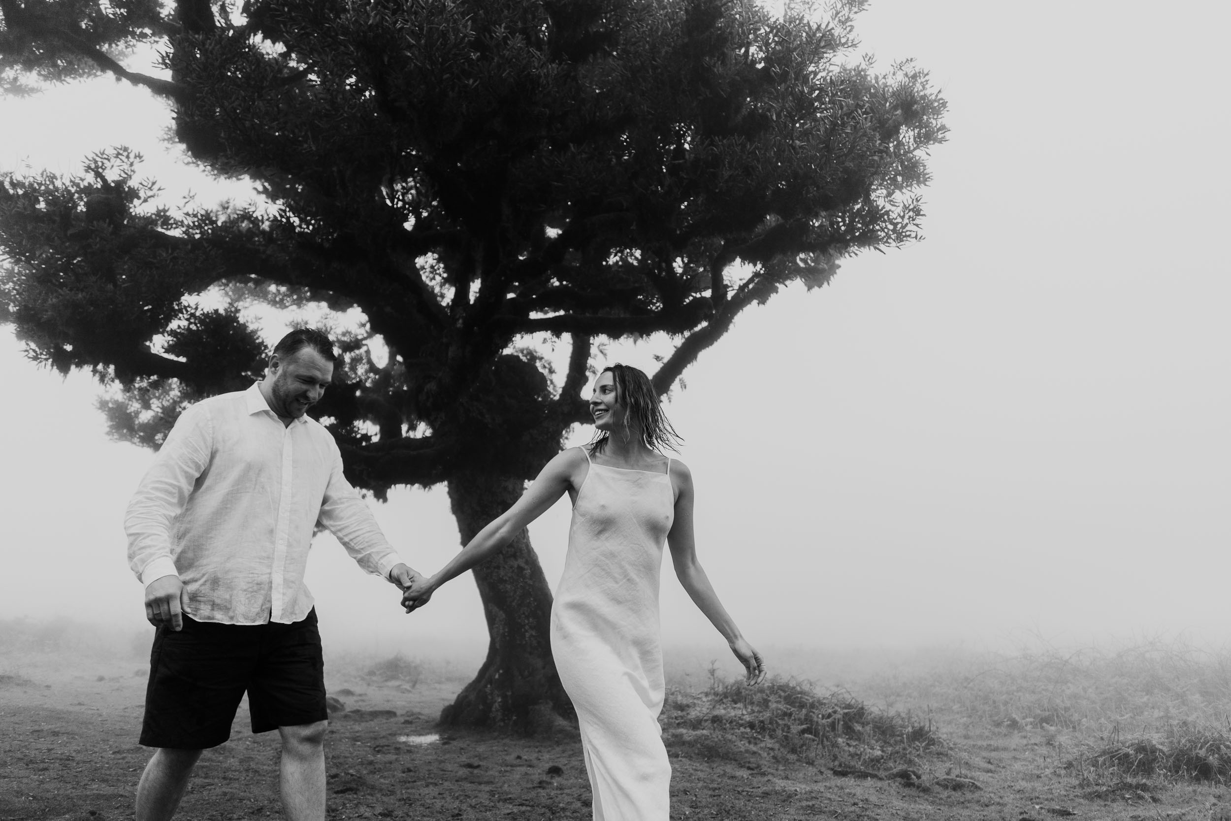 Couple in white linen under ancient laurel trees in dense afternoon fog, Fanal Forest, Madeira
