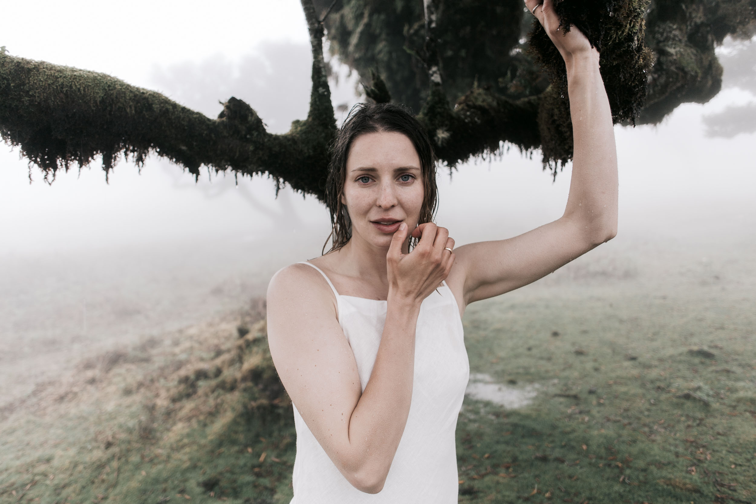 White-linen couple by a moss-covered trunk in the fog of Fanal Forest, Madeira