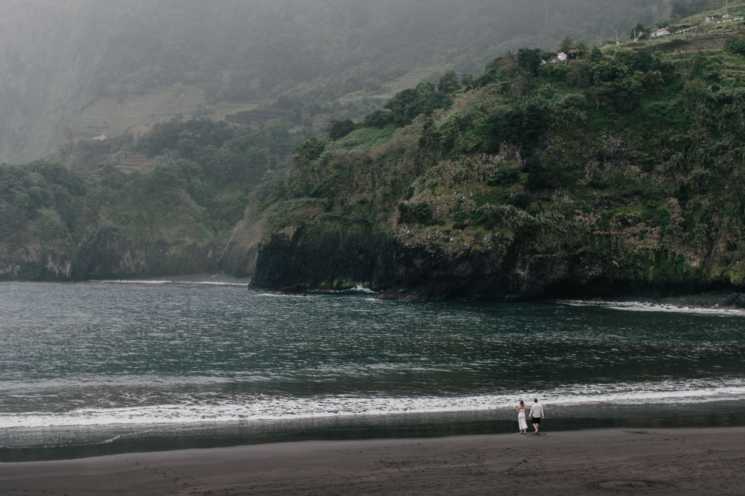 Empty stretch of black sand and Atlantic waves, the couple as silhouettes near the surf, Madeira