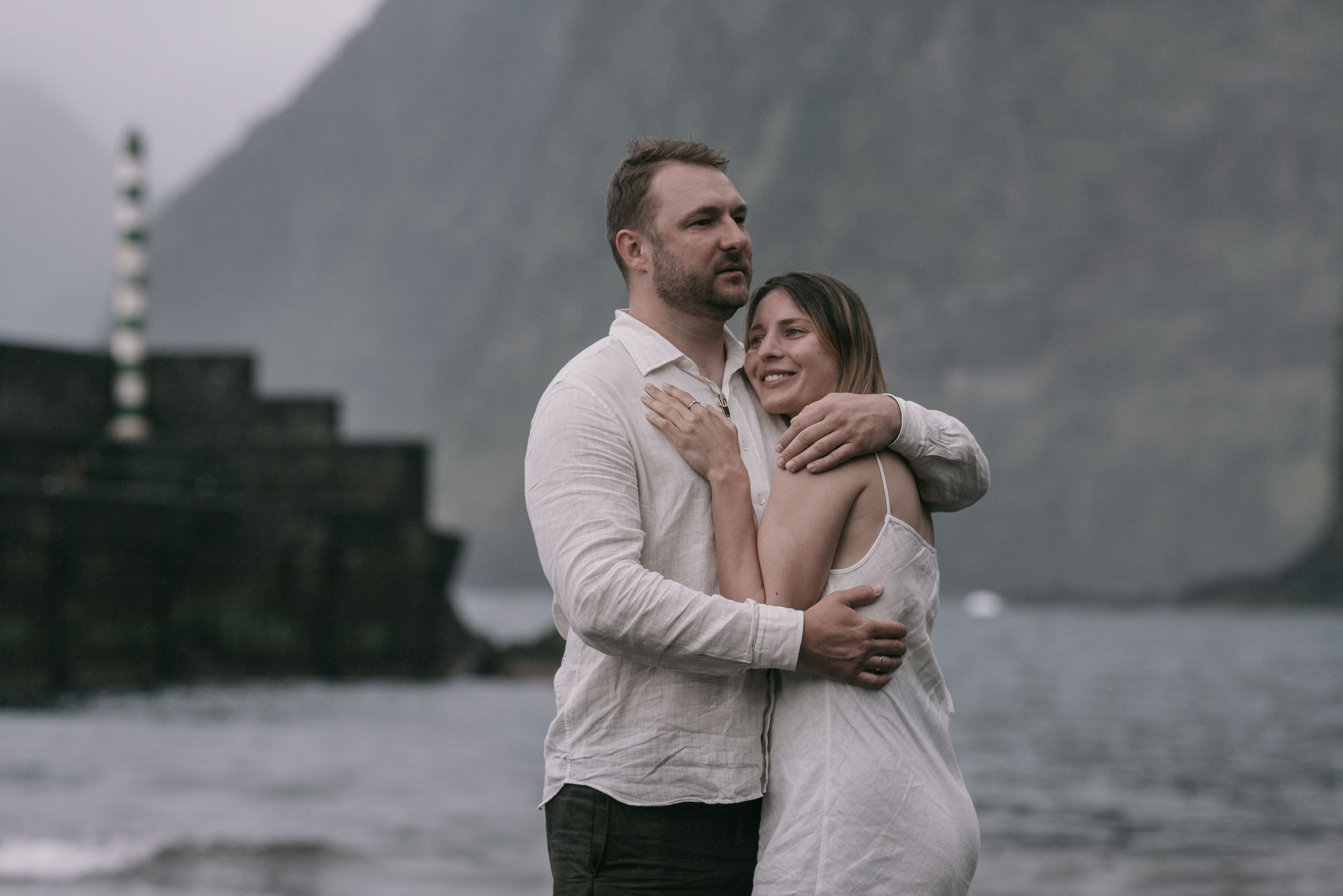 Couple small in the frame of a black sand cove, sheer cliffs on both sides, Atlantic surf, north Madeira
