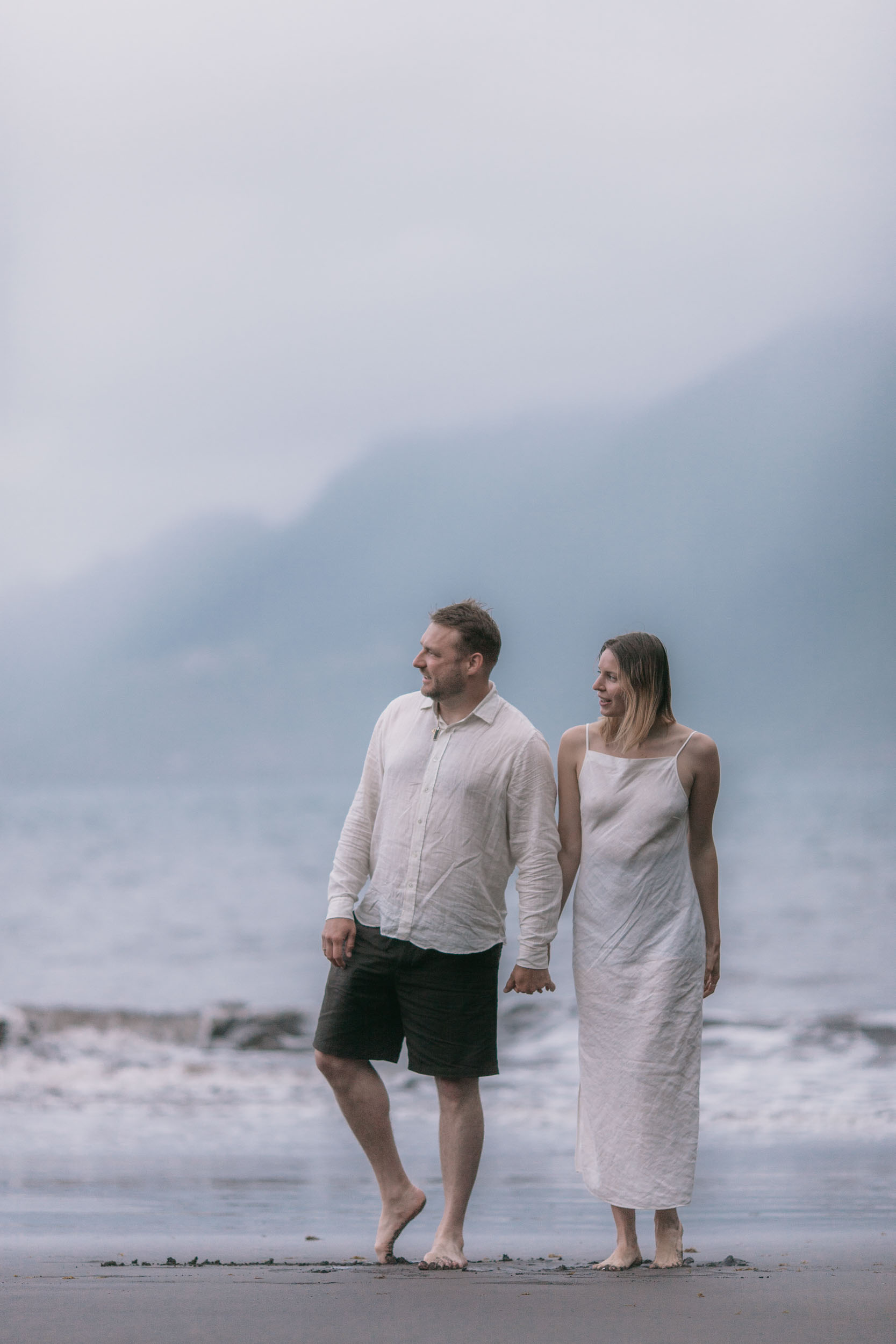 Wide pejzaze of a dark beach with the couple walking at the waterline, dramatic cliffs behind, north Madeira
