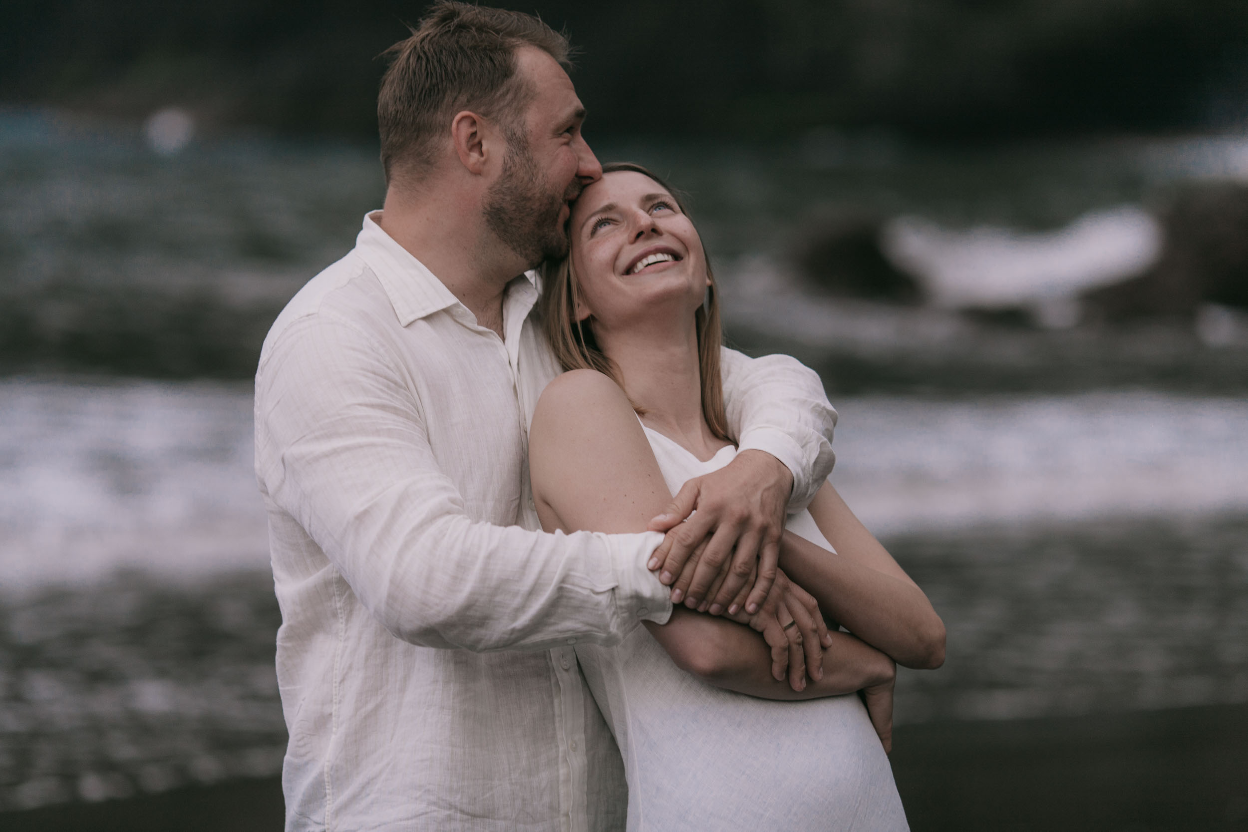 Close embrace on a black sand beach, the Atlantic and dark cliffs behind, white linen, Madeira