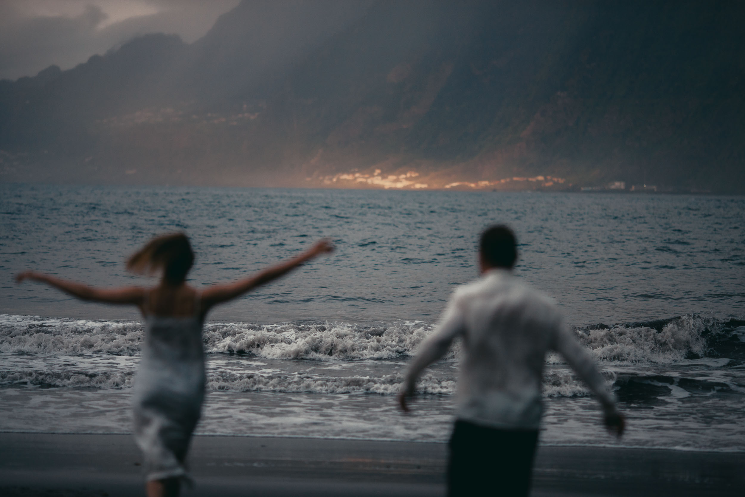 Couple running on a dark beach at last light, ocean spray, Madeira