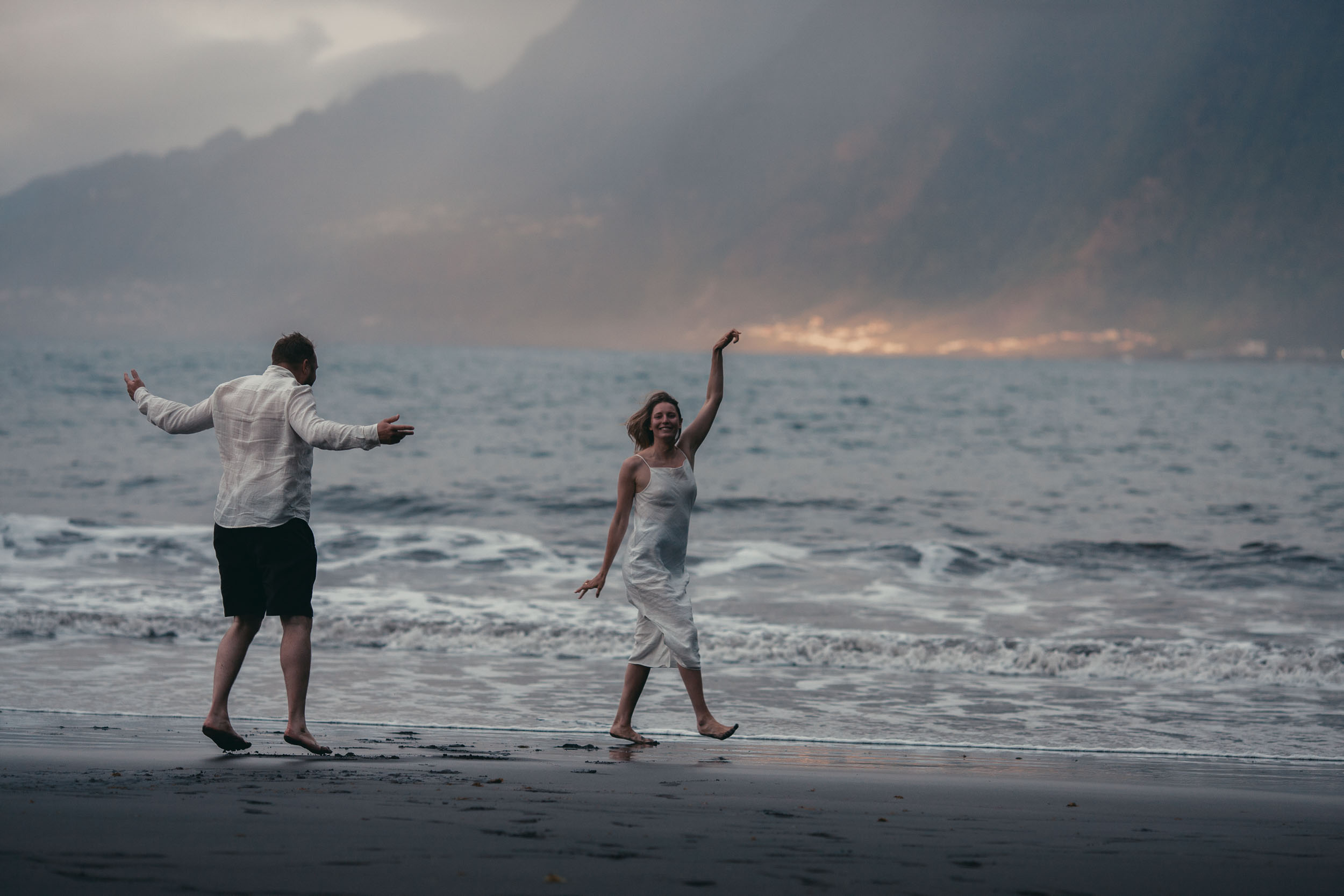 Silhouettes on a black sand beach at sunset, the couple running through the surf, north Madeira