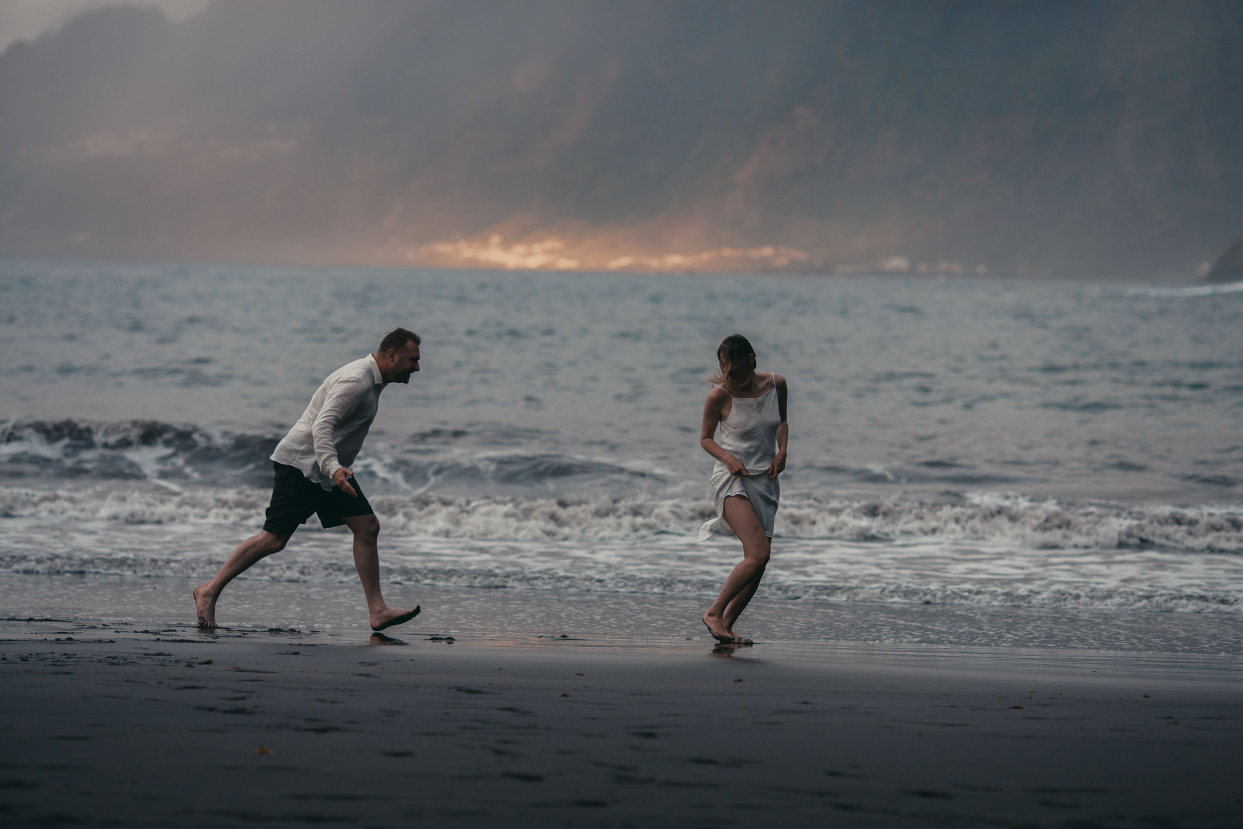 Couple running on a dark beach at last light, ocean spray, Madeira