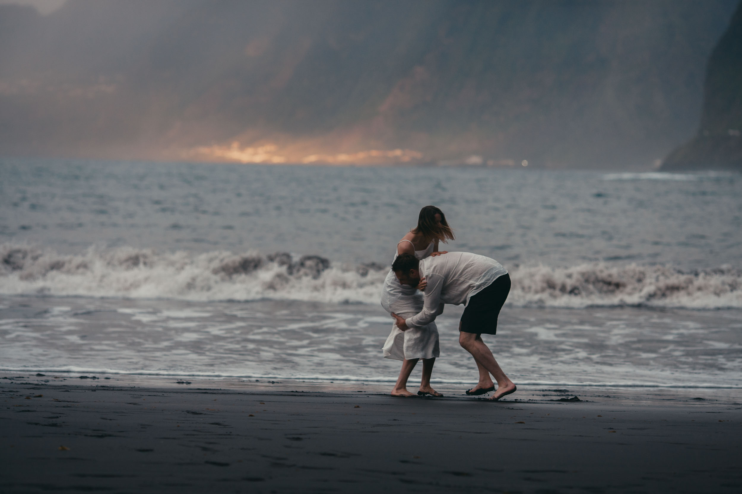 Silhouettes on a black sand beach at sunset, the couple running through the surf, north Madeira