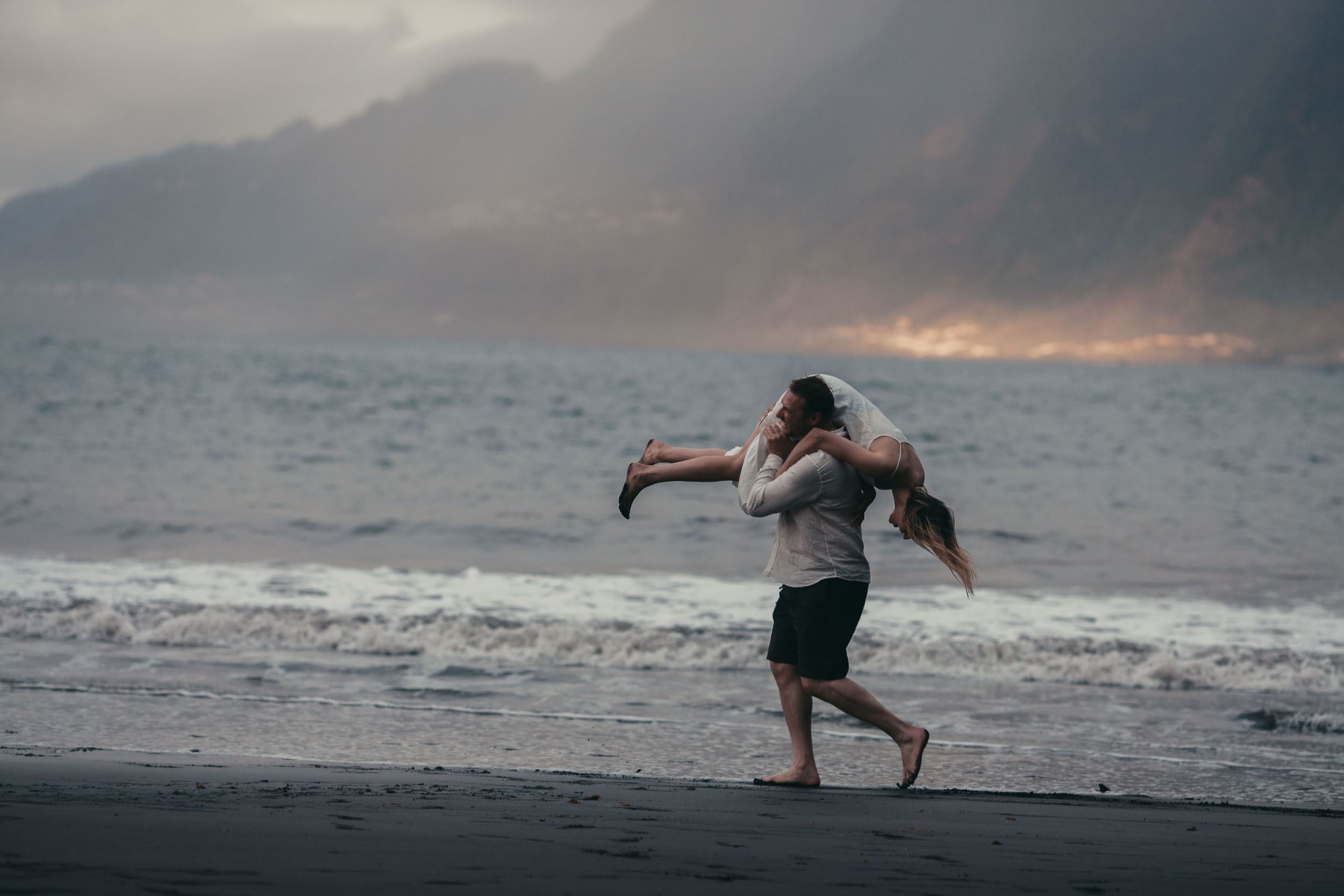 Couple playing in the shallows at golden hour, splash kicked up, dark cliffs behind, Madeira