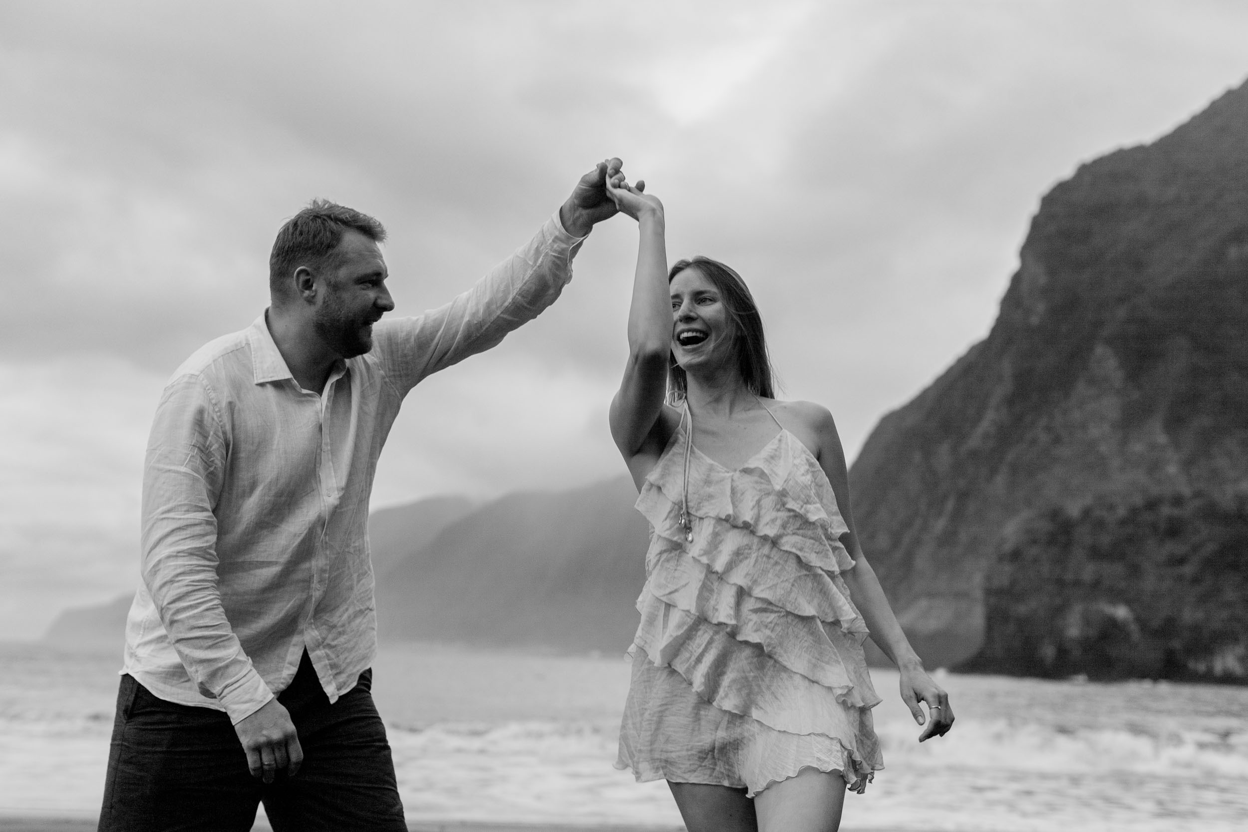 Black and white. Couple at the edge of the Atlantic, dramatic cliffs filling the frame, Madeira