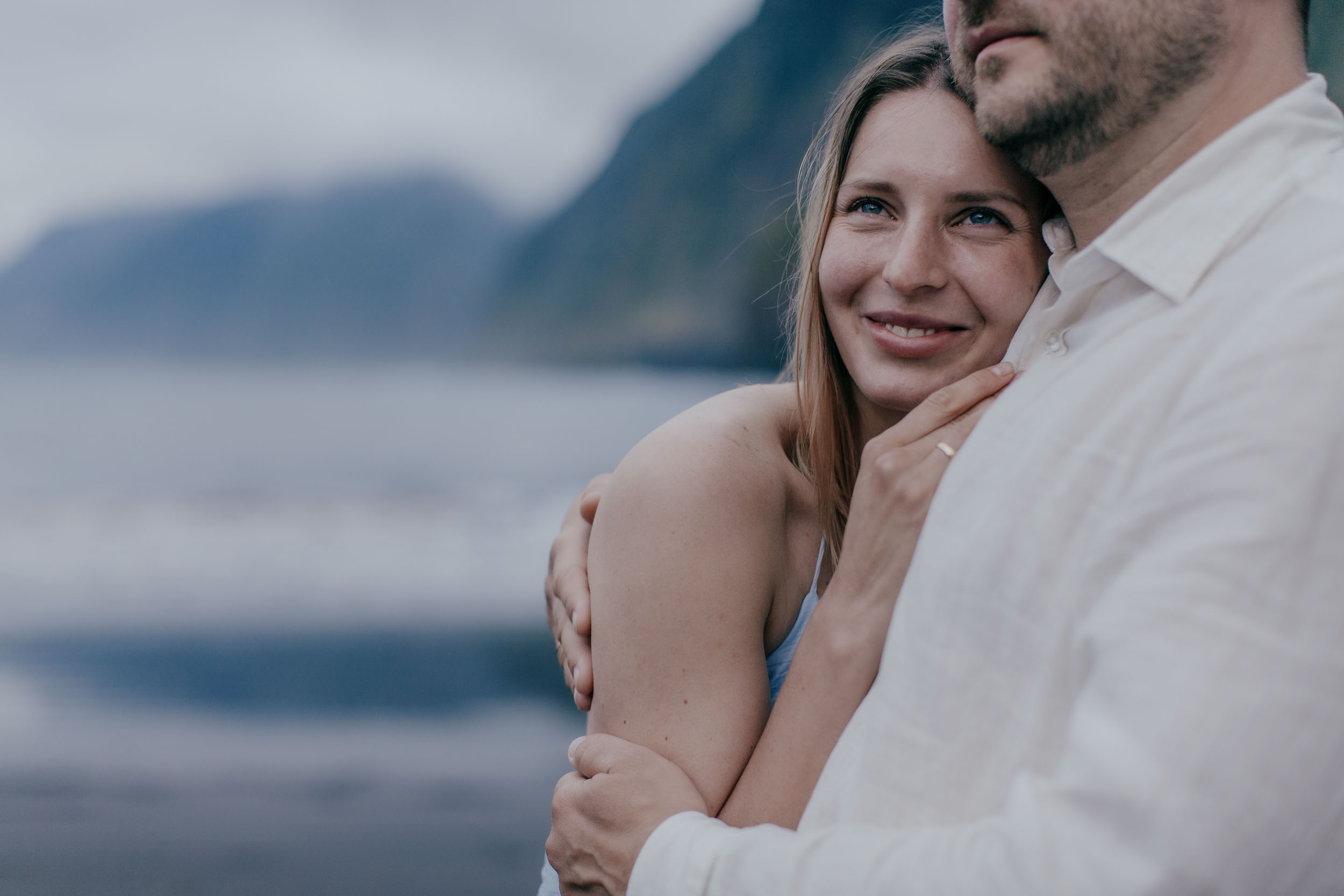 Engagement rings on both hands, soft focus on the couple behind, dramatic Madeira cliffs