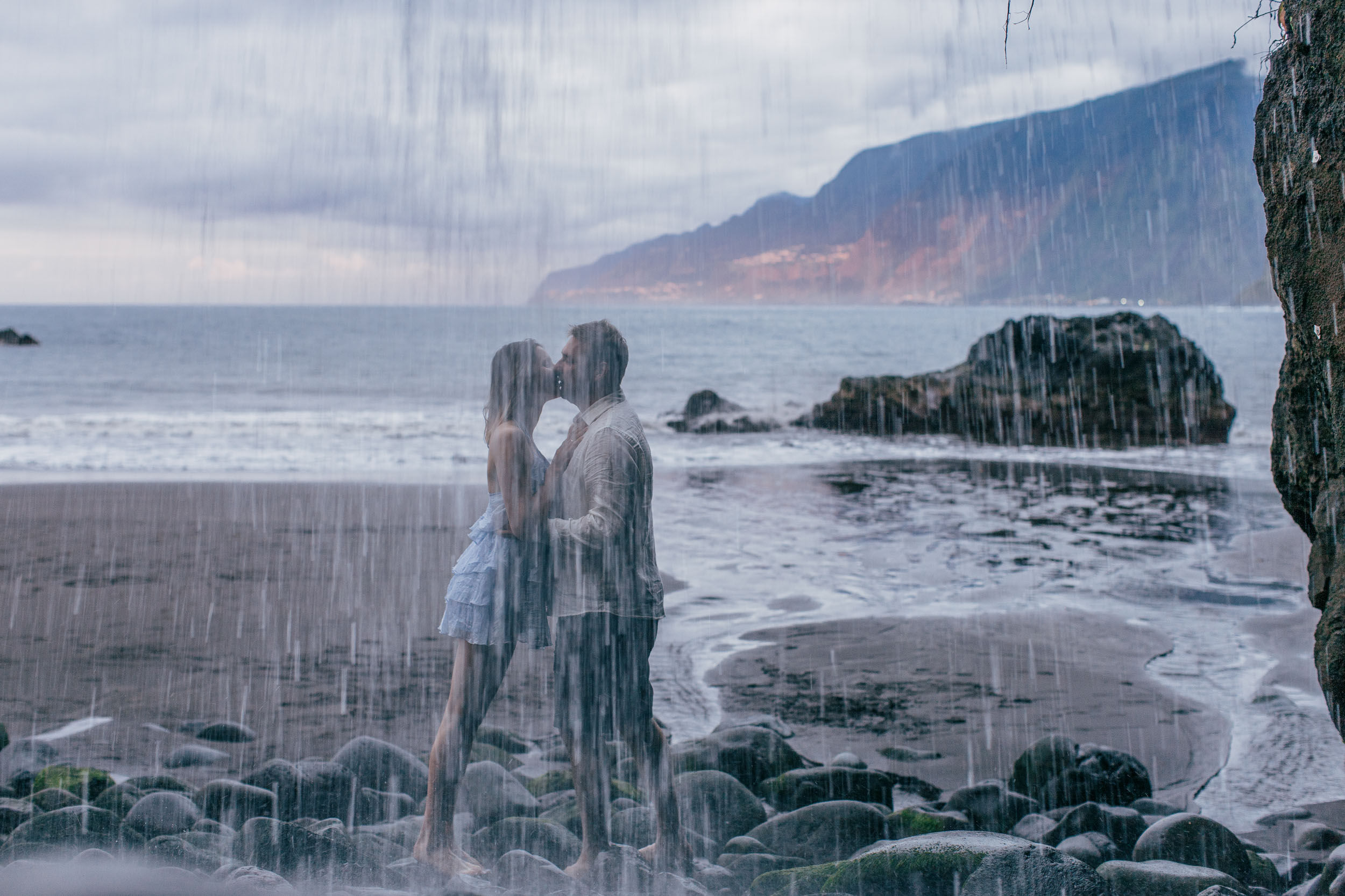 Couple framed by towering volcanic rocks on a dark beach, north Madeira coast