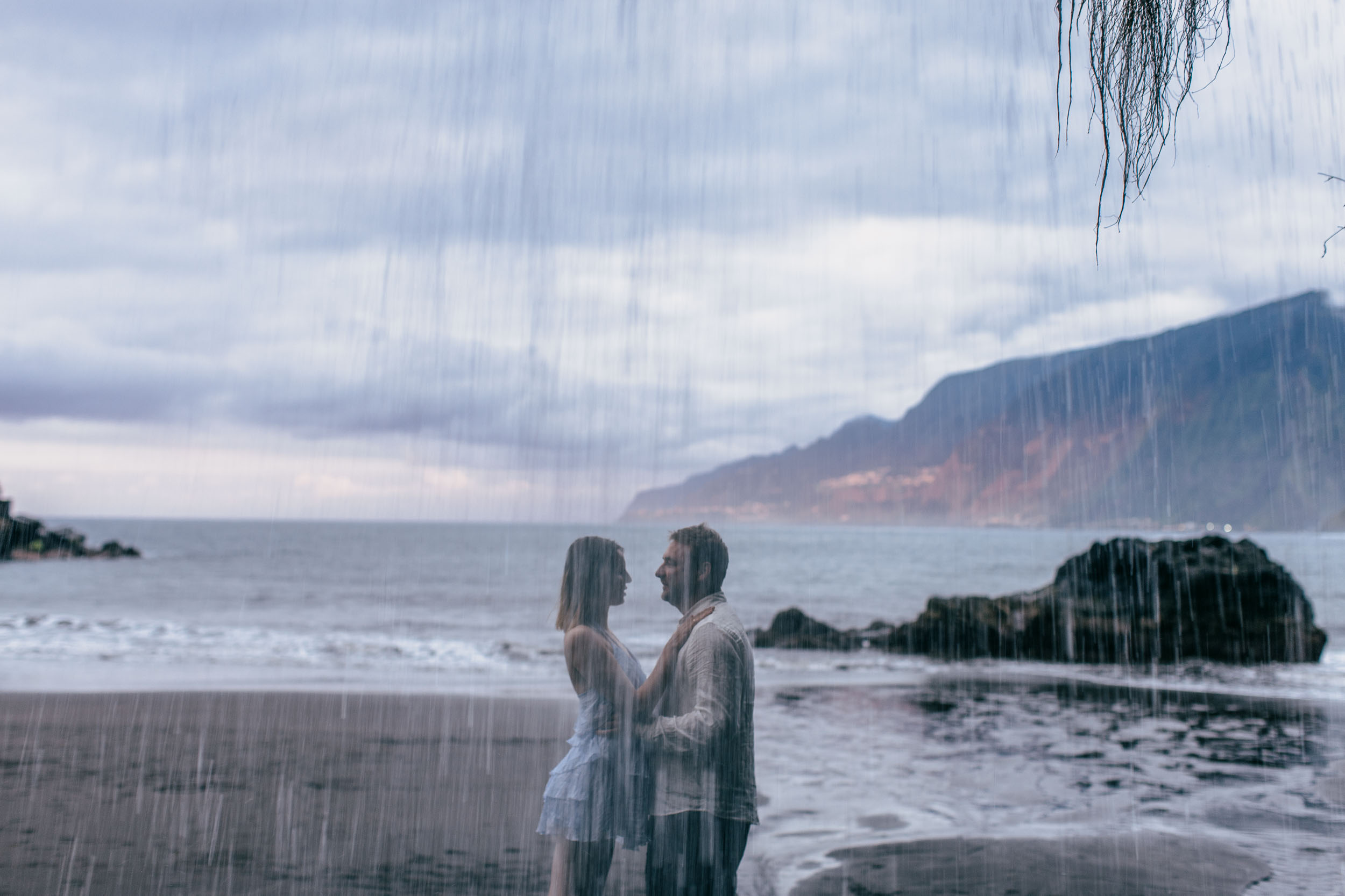 Dramatic basalt stacks rising from the dark sand, the couple small in the frame, Madeira