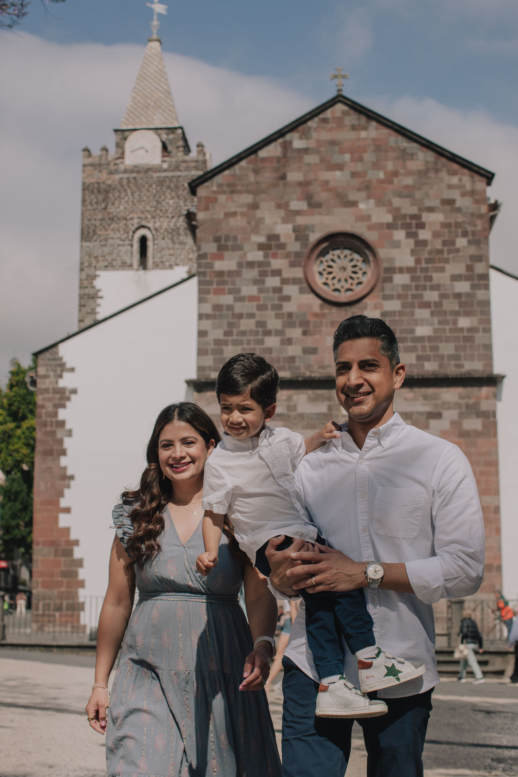 Family of three in front of Funchal Cathedral, Madeira. mother in blue dress, father holding young son