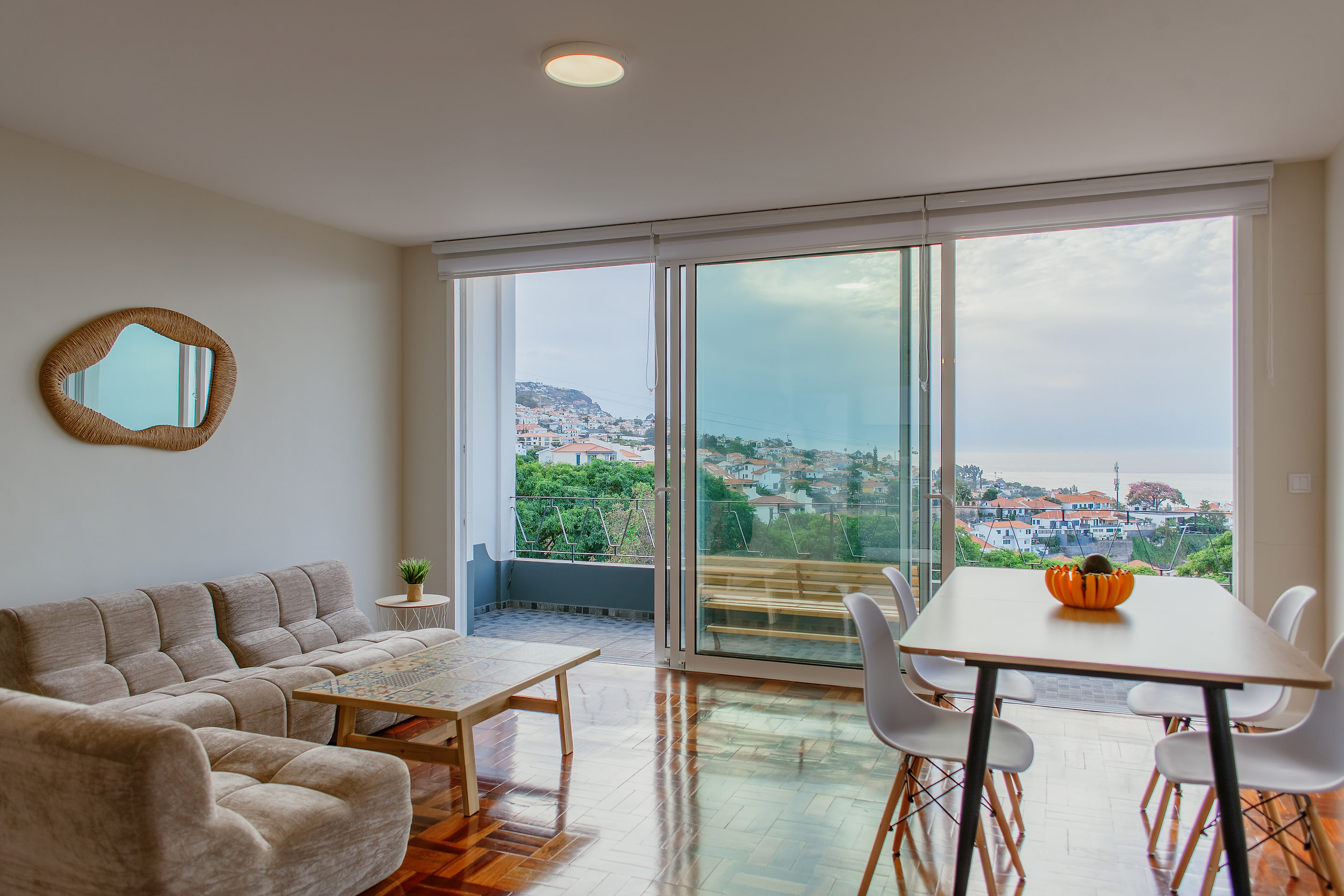 Living room of a three-bedroom apartment in Funchal, sofa and dining table, glass doors open onto the balcony and the ocean