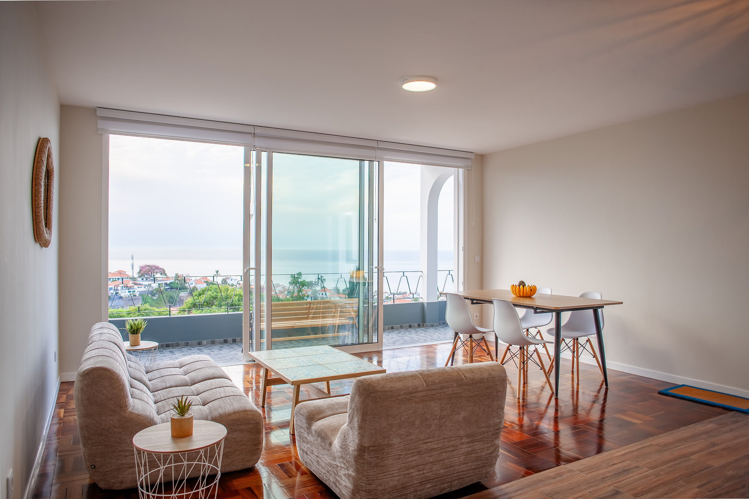 Living room with a tiled coffee table and parquet floor, the balcony and the sea through floor-to-ceiling glass, apartment in Funchal