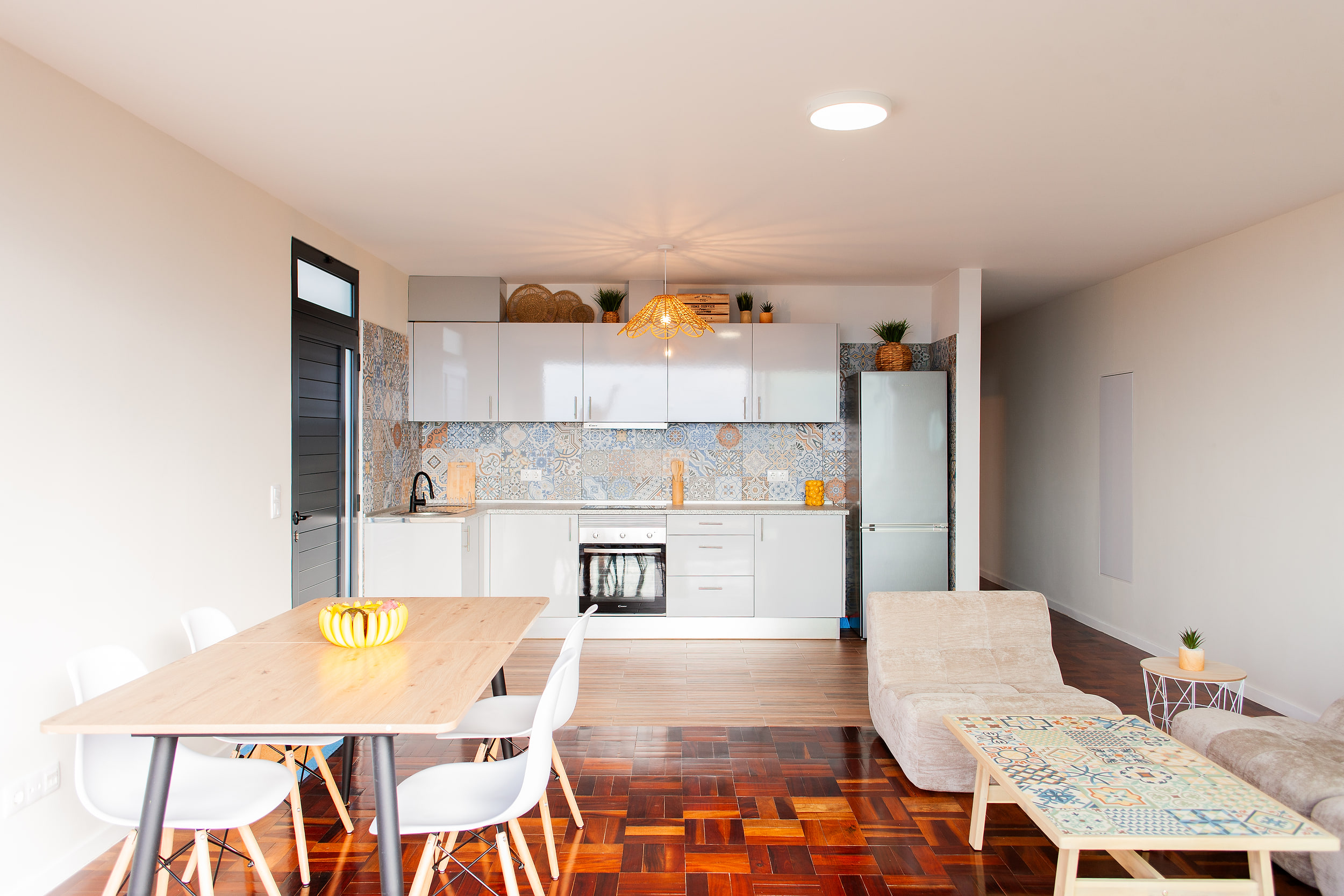 Open-plan kitchen and dining area with white cabinets, patterned tiles and a wicker lamp over the counter