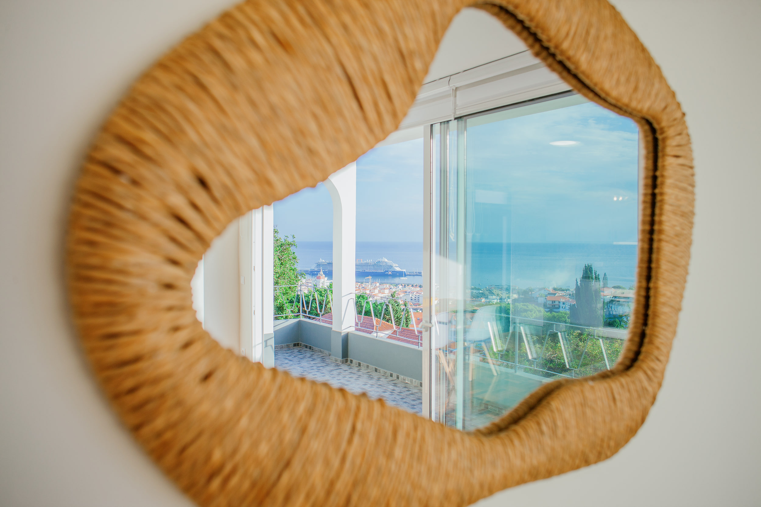 Wicker mirror reflecting the balcony arches and a cruise ship in Funchal harbour
