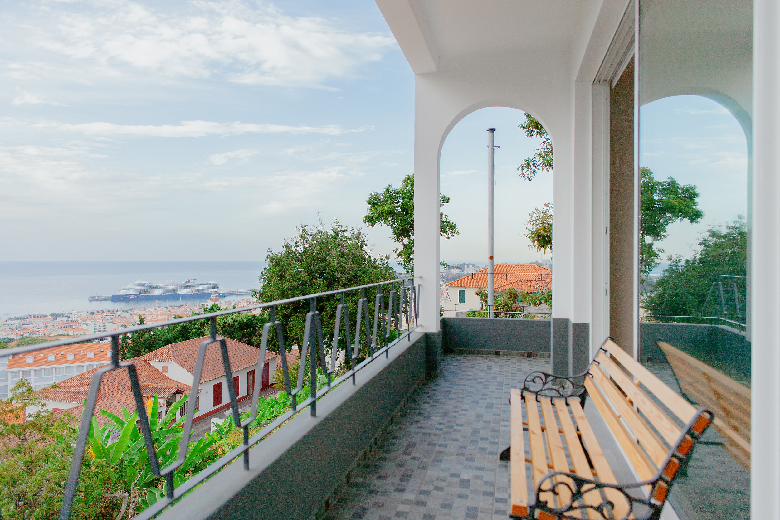 Long balcony with white arches and two benches, a cruise ship in the bay beyond