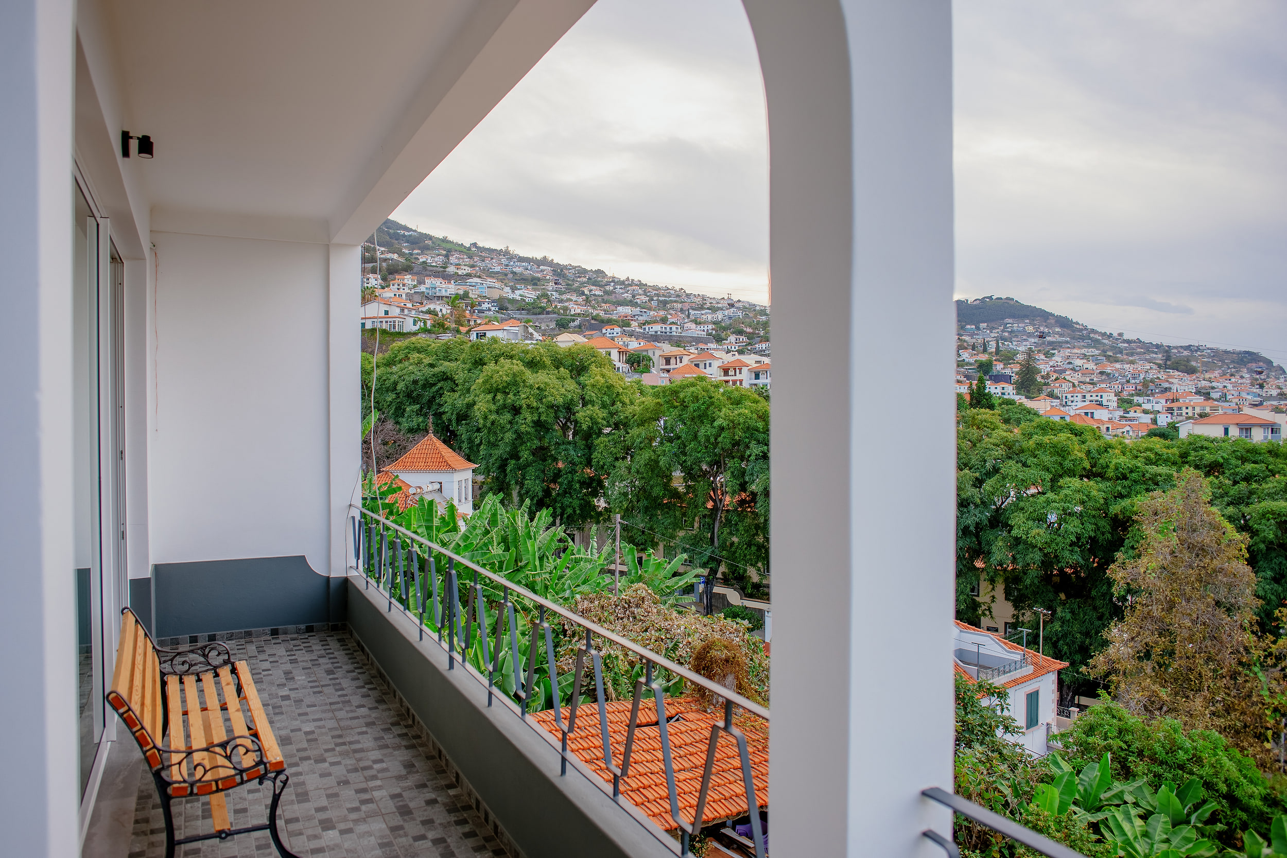 Arched balcony with a bench, banana plants below and houses on the Funchal hillside
