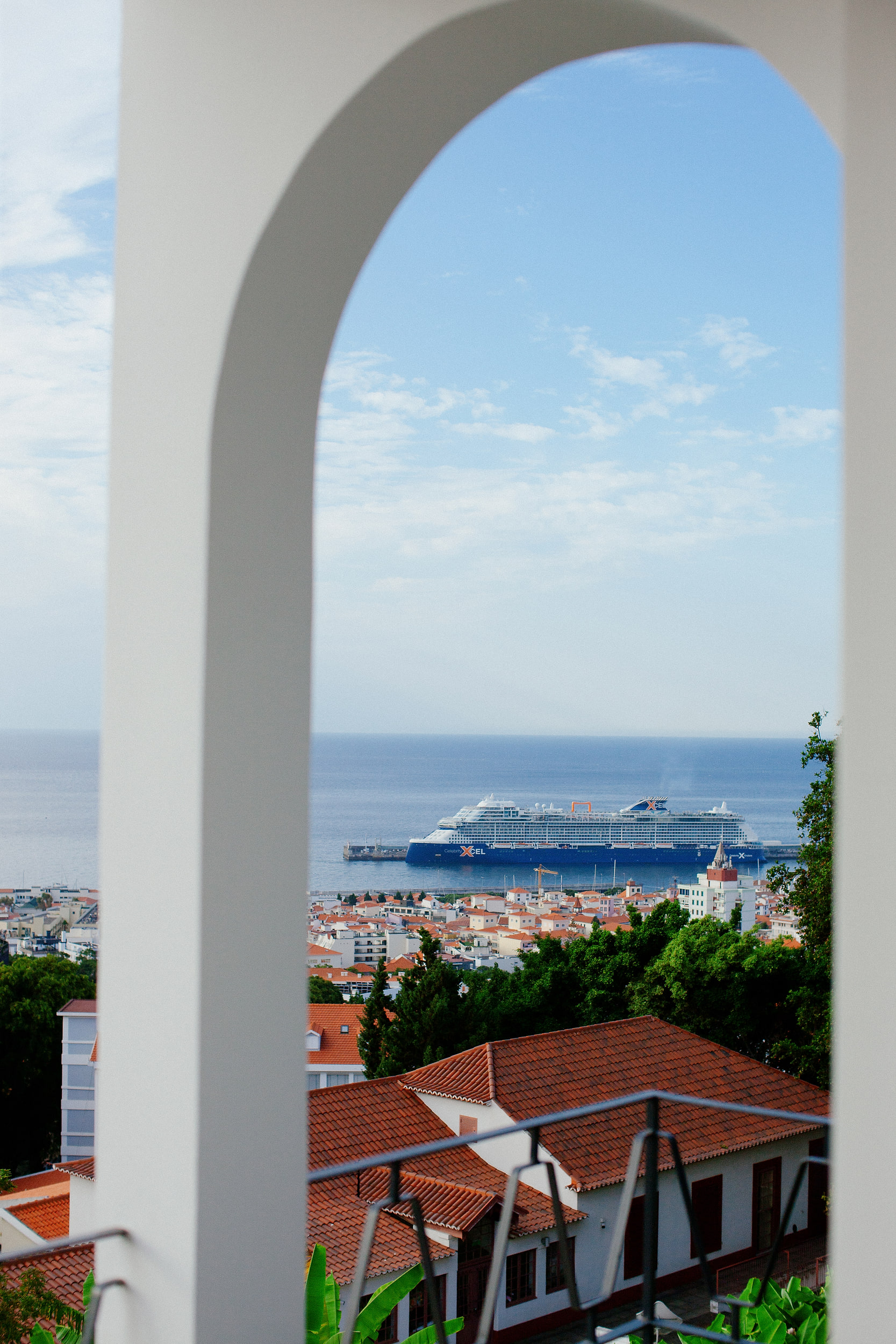 White arch framing Funchal harbour, a cruise ship at the pier and red roofs below