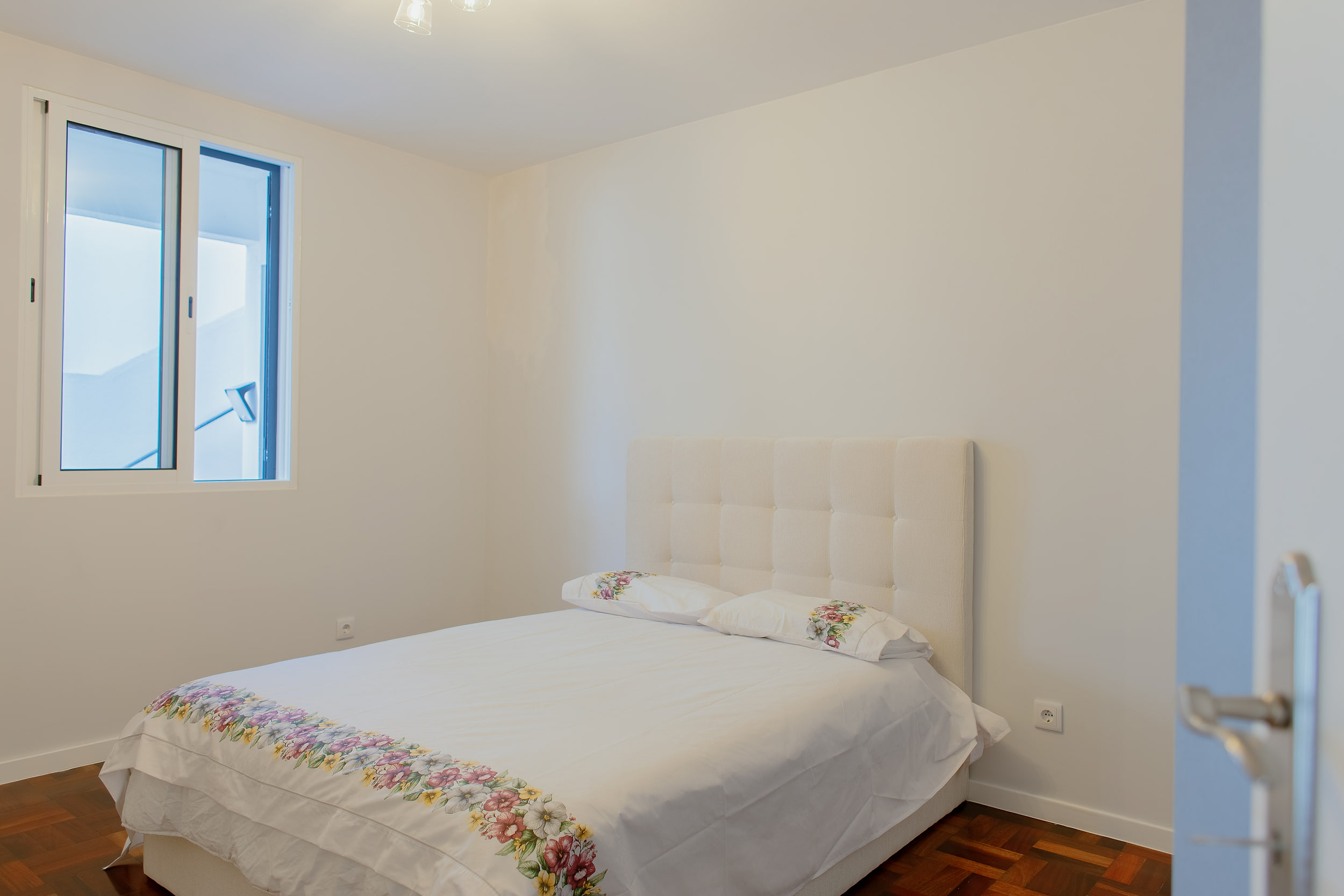 Double bedroom with a white tufted headboard and bedding with a floral border