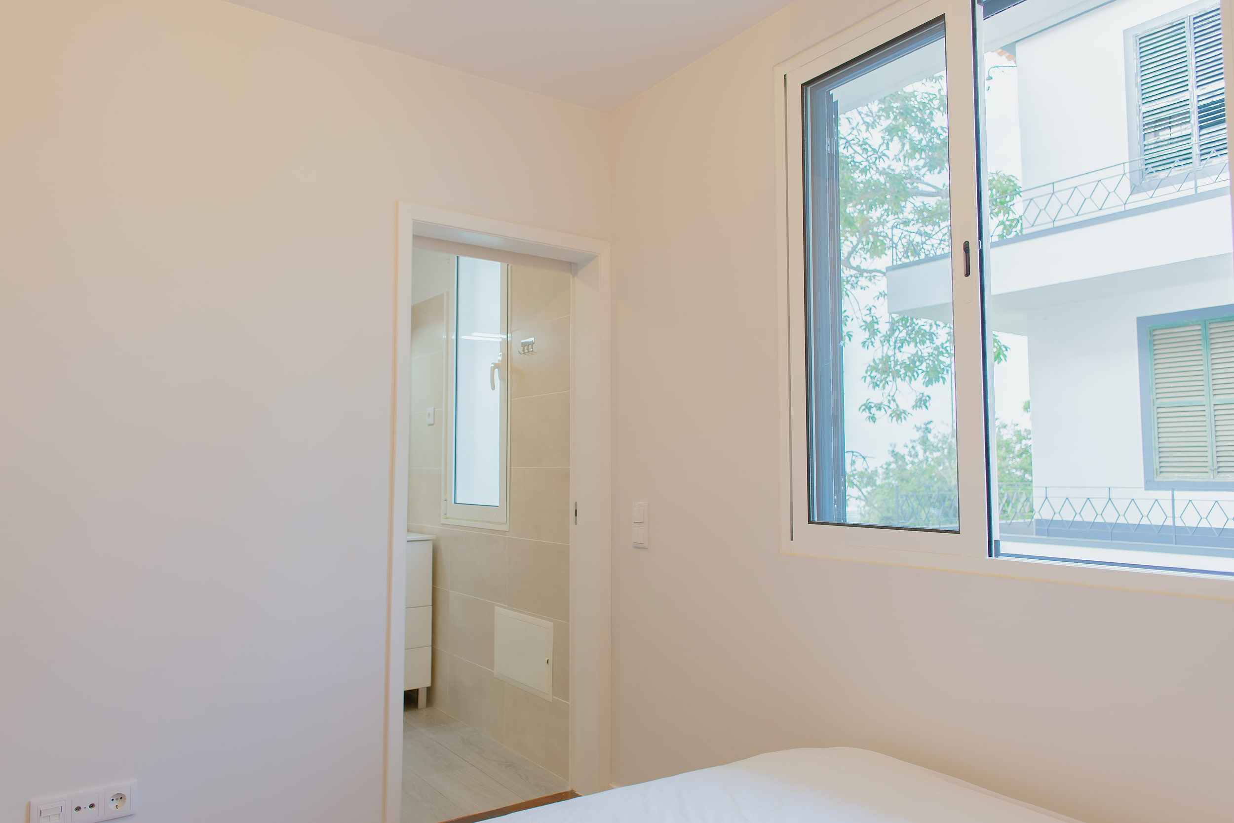 Bedroom window onto a white neighbouring building, a door open to the bathroom