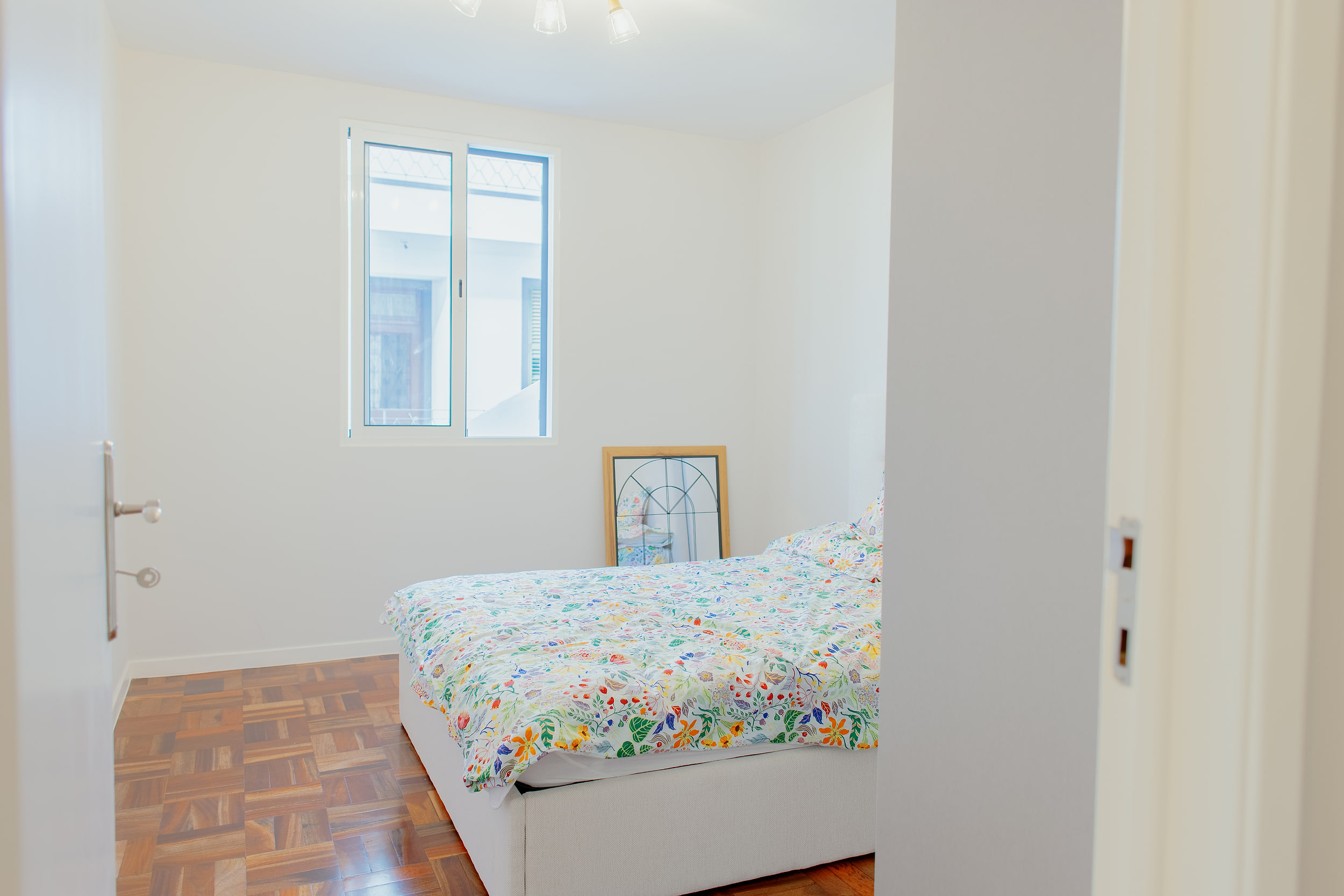 Bedroom seen from the doorway, a floral duvet and a framed mirror leaning on the wall