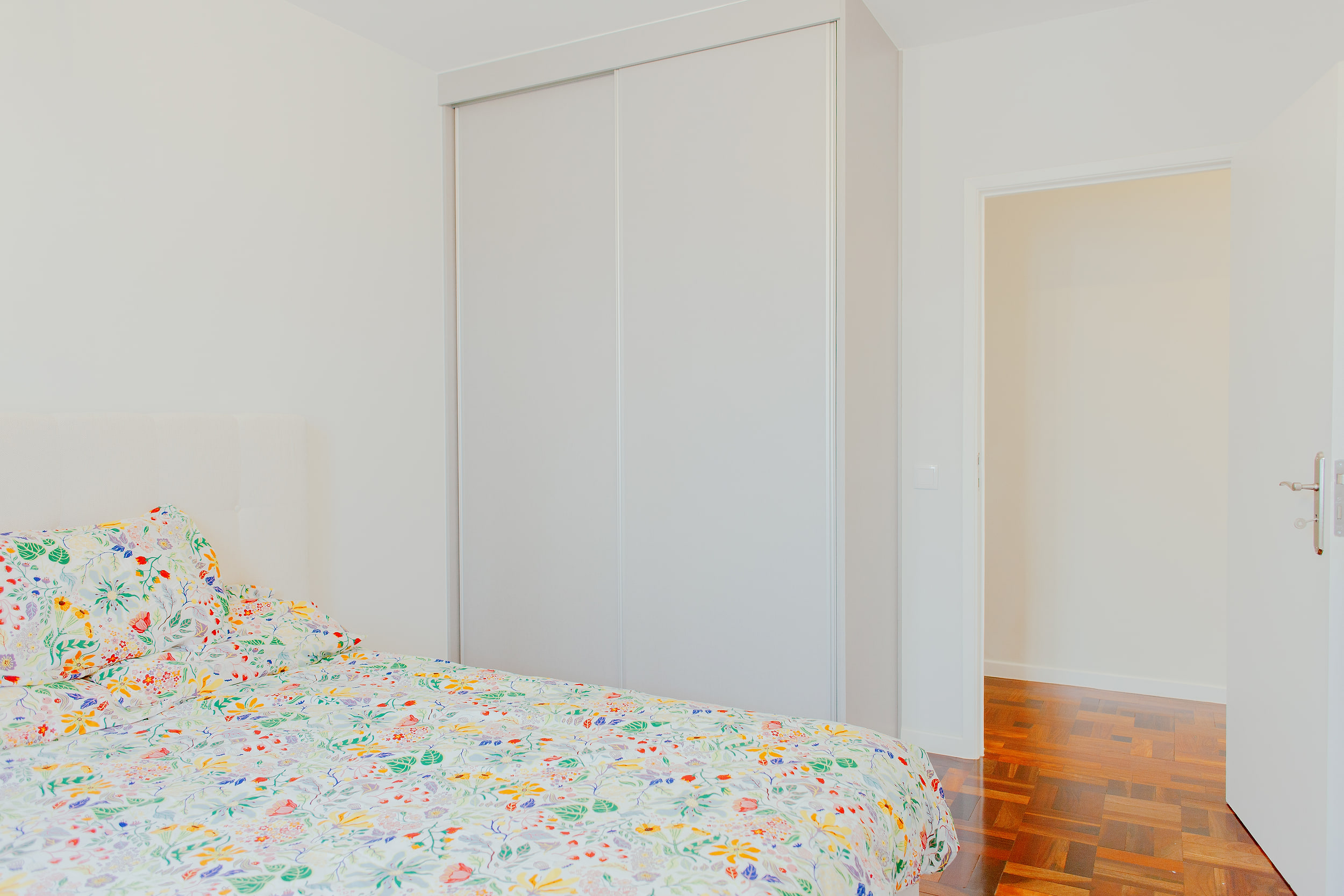 Bedroom with floral bedding, a built-in sliding wardrobe and the door open to the corridor