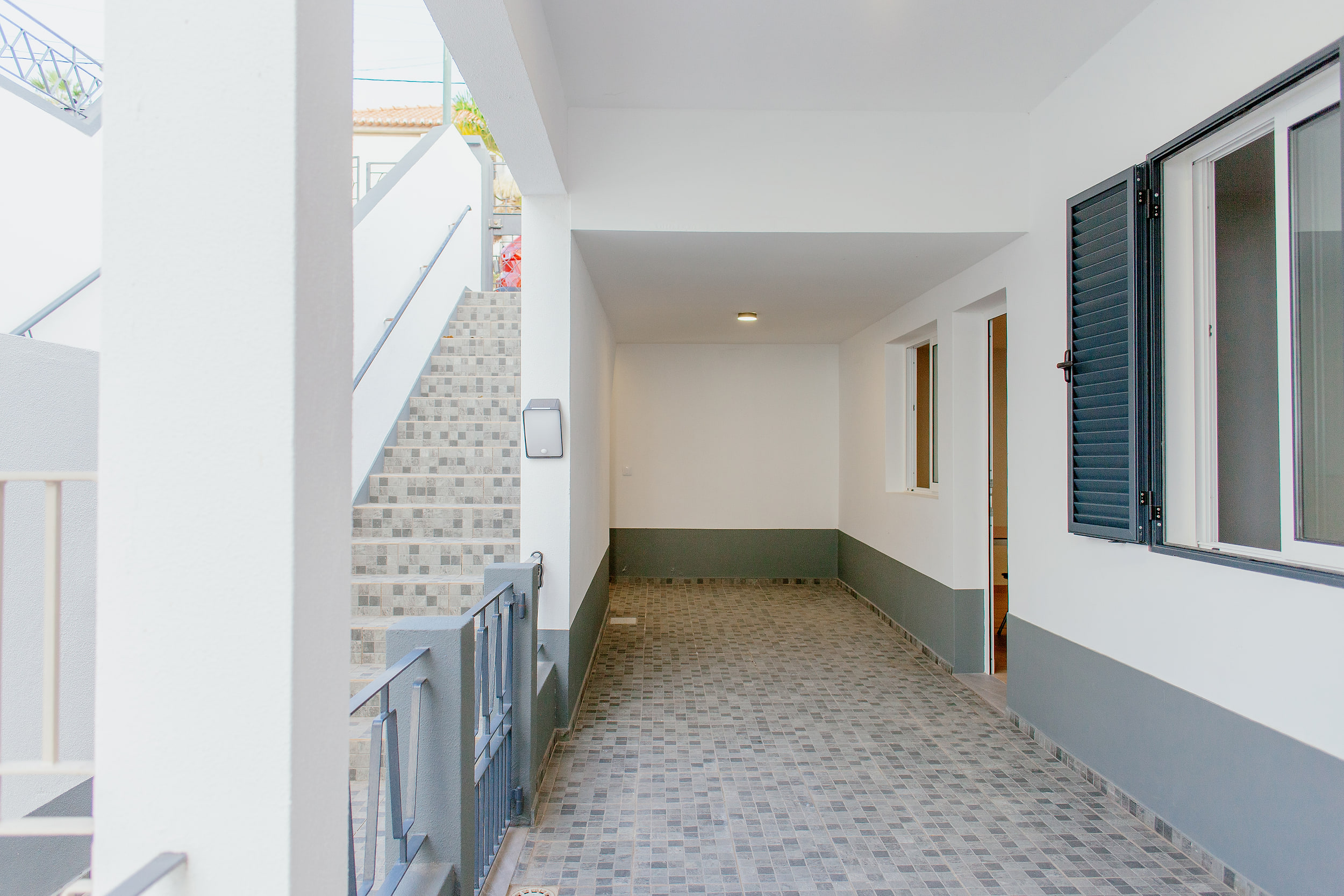 Covered ground-floor area with grey mosaic tiles and a stairway up to the street