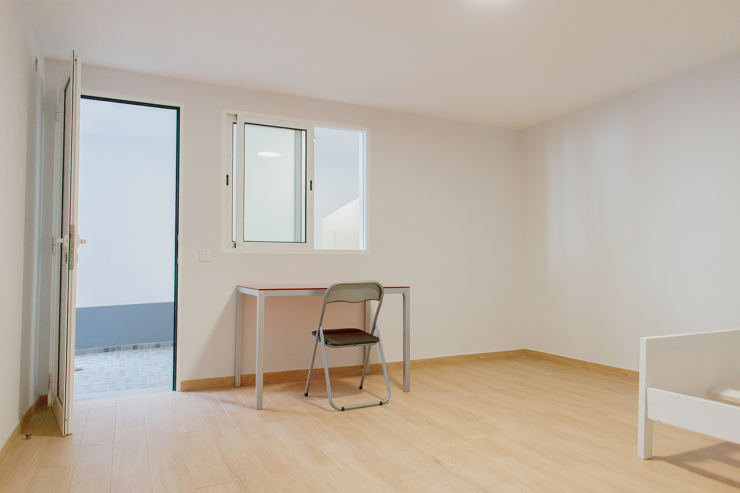 Lower room with a desk and a folding chair, the door open to a tiled patio