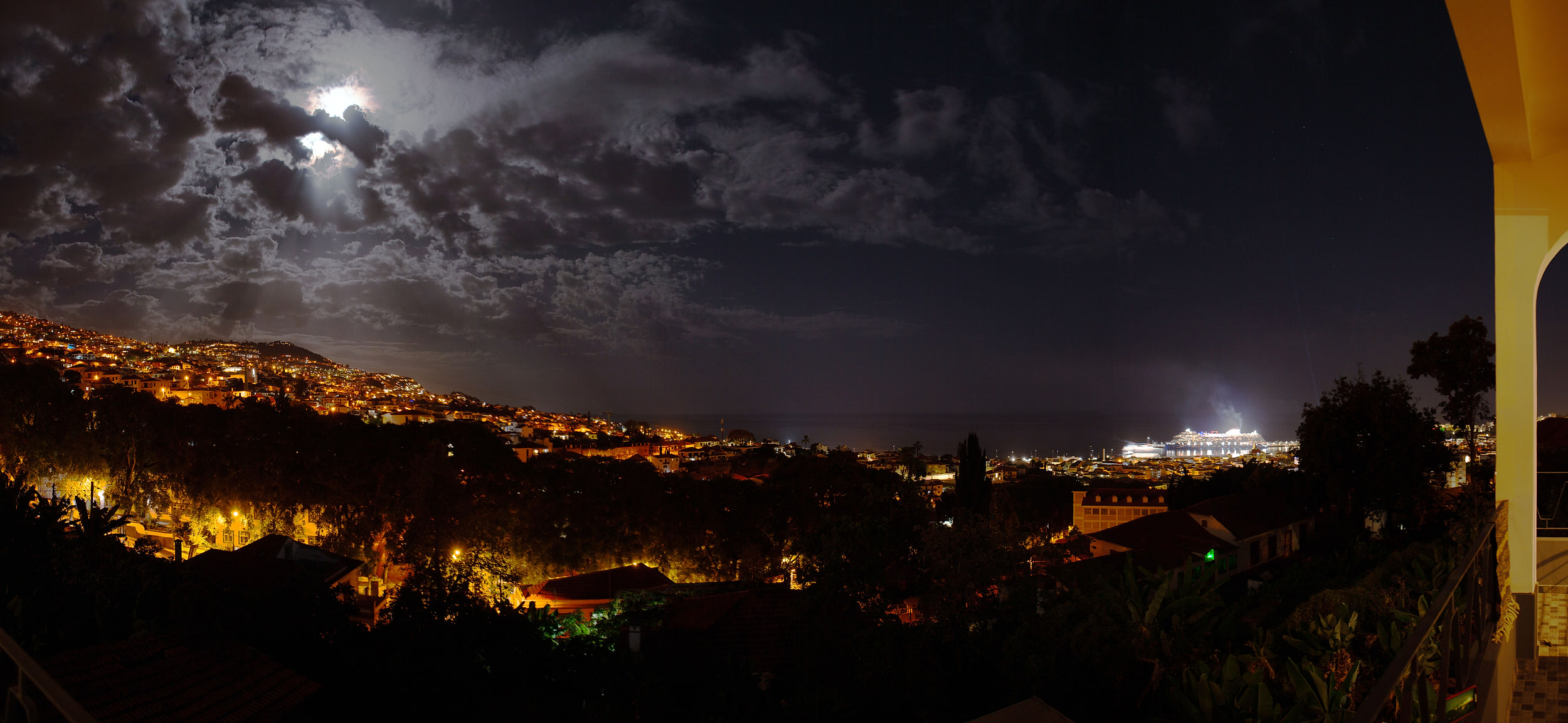 Night panorama with the full moon behind clouds, the lights of Funchal and the cruise ship in the bay