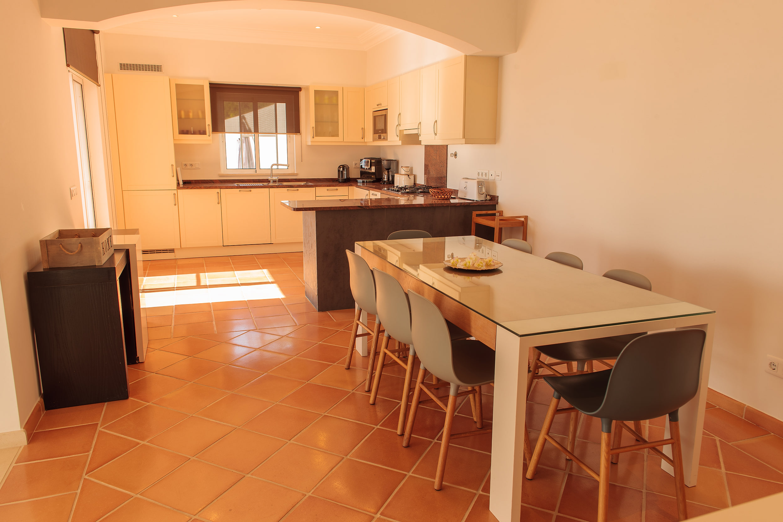 Long dining table under an arch, the cream kitchen and breakfast bar beyond