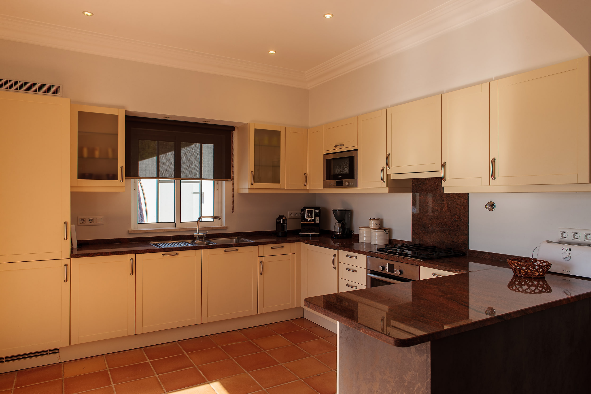Cream kitchen with granite worktops, a gas hob and a window with a dark blind