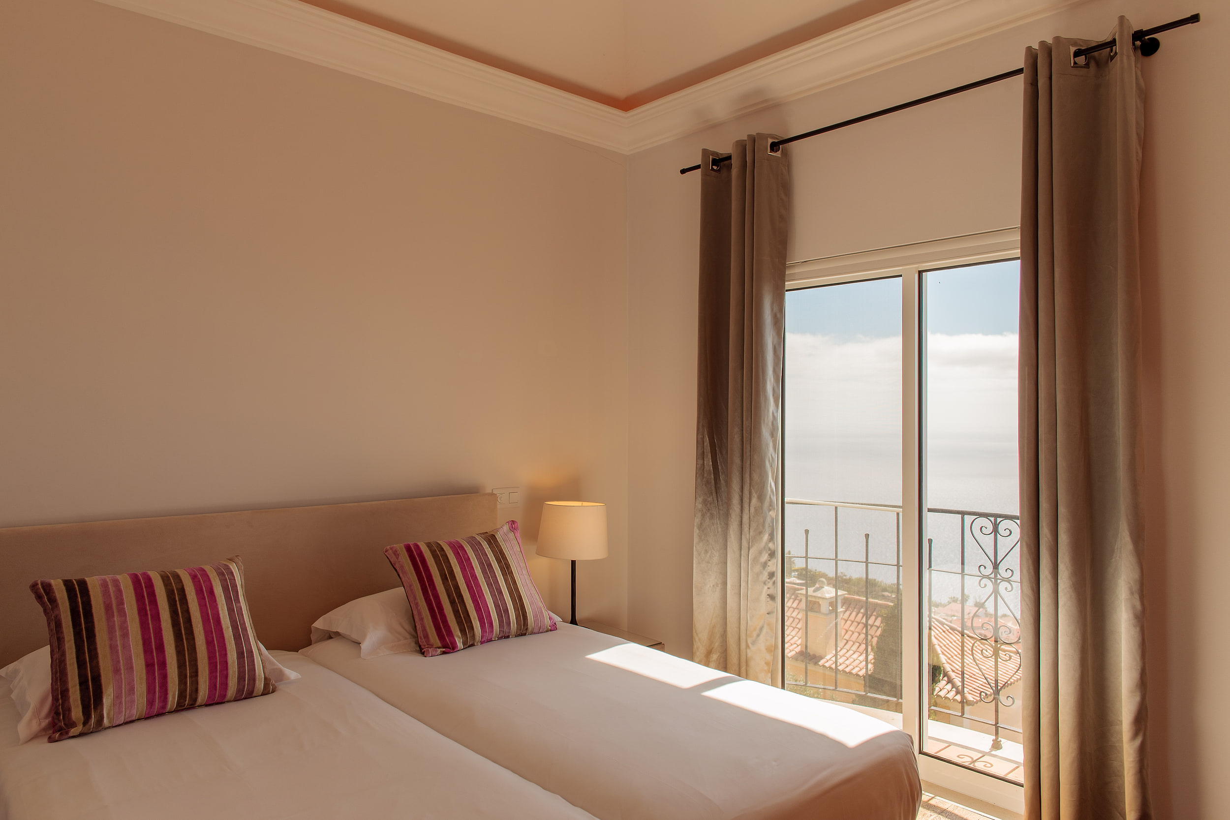 Twin bedroom with striped cushions and a lamp, the balcony door open onto the ocean