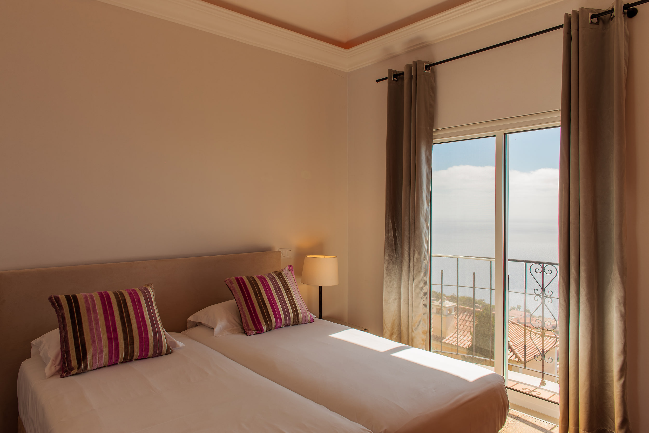 The same twin bedroom from a wider angle, sun on the beds and long curtains framing the sea