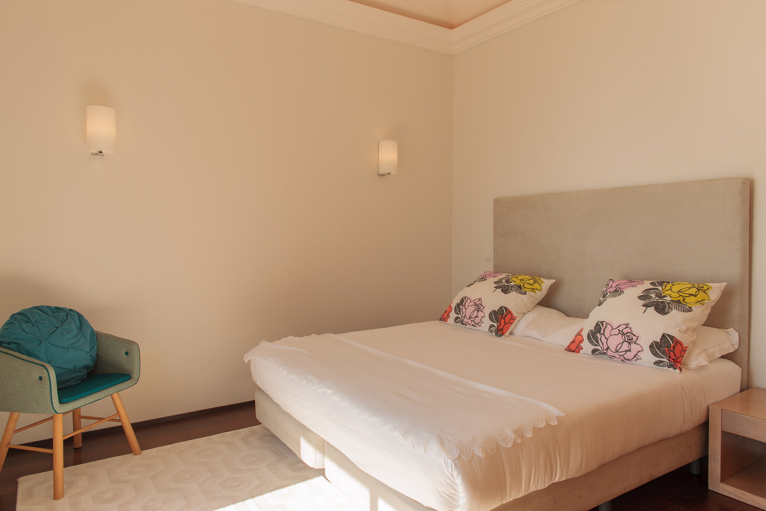Double bedroom with a grey headboard, rose print cushions and two wall lights