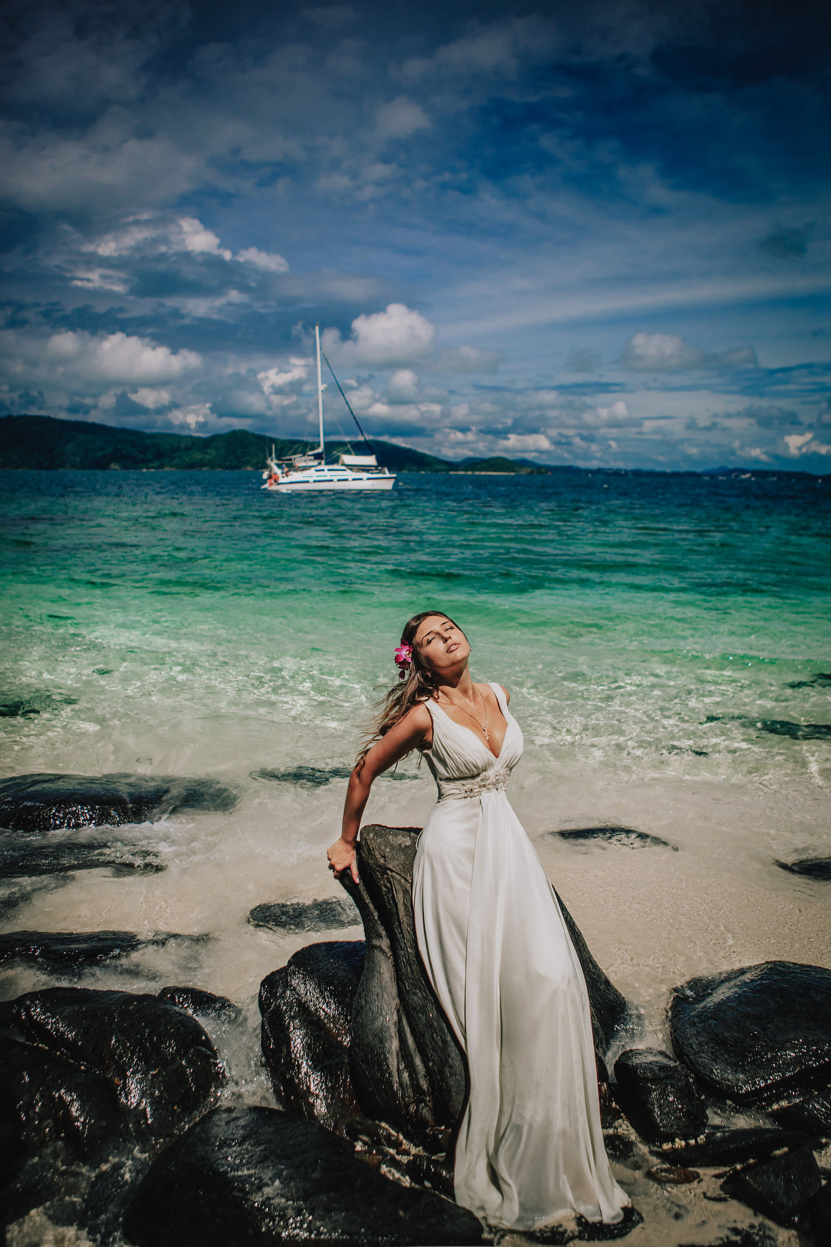 Bride standing on dark rocks at the waterline in a flowing dress