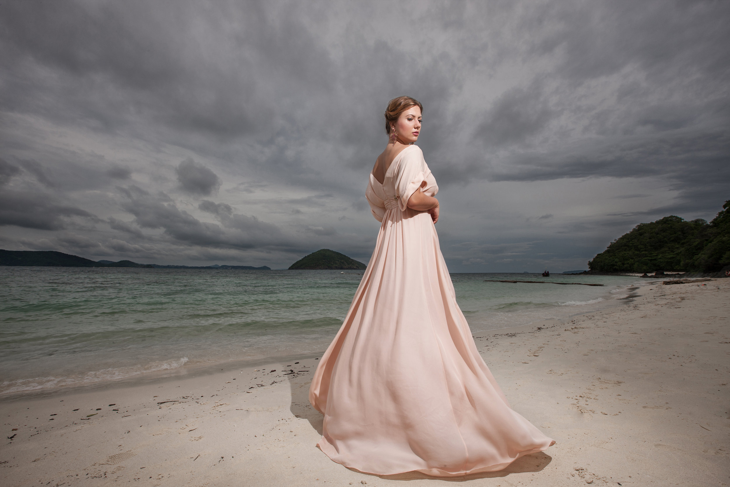 Bride in a long dress on an empty beach under a heavy grey sky