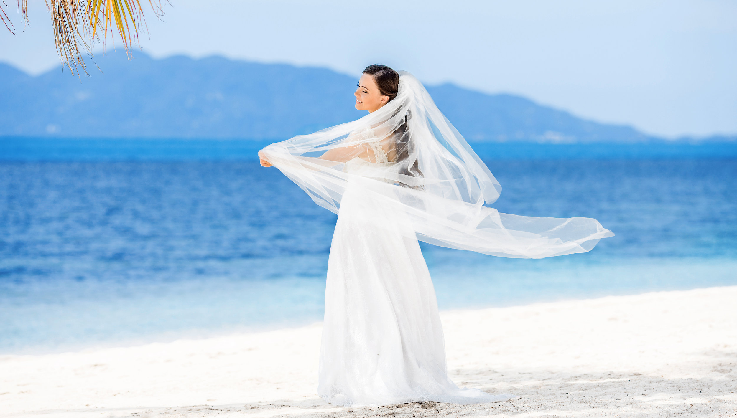 Bride on the shore with her veil pulled sideways by the wind
